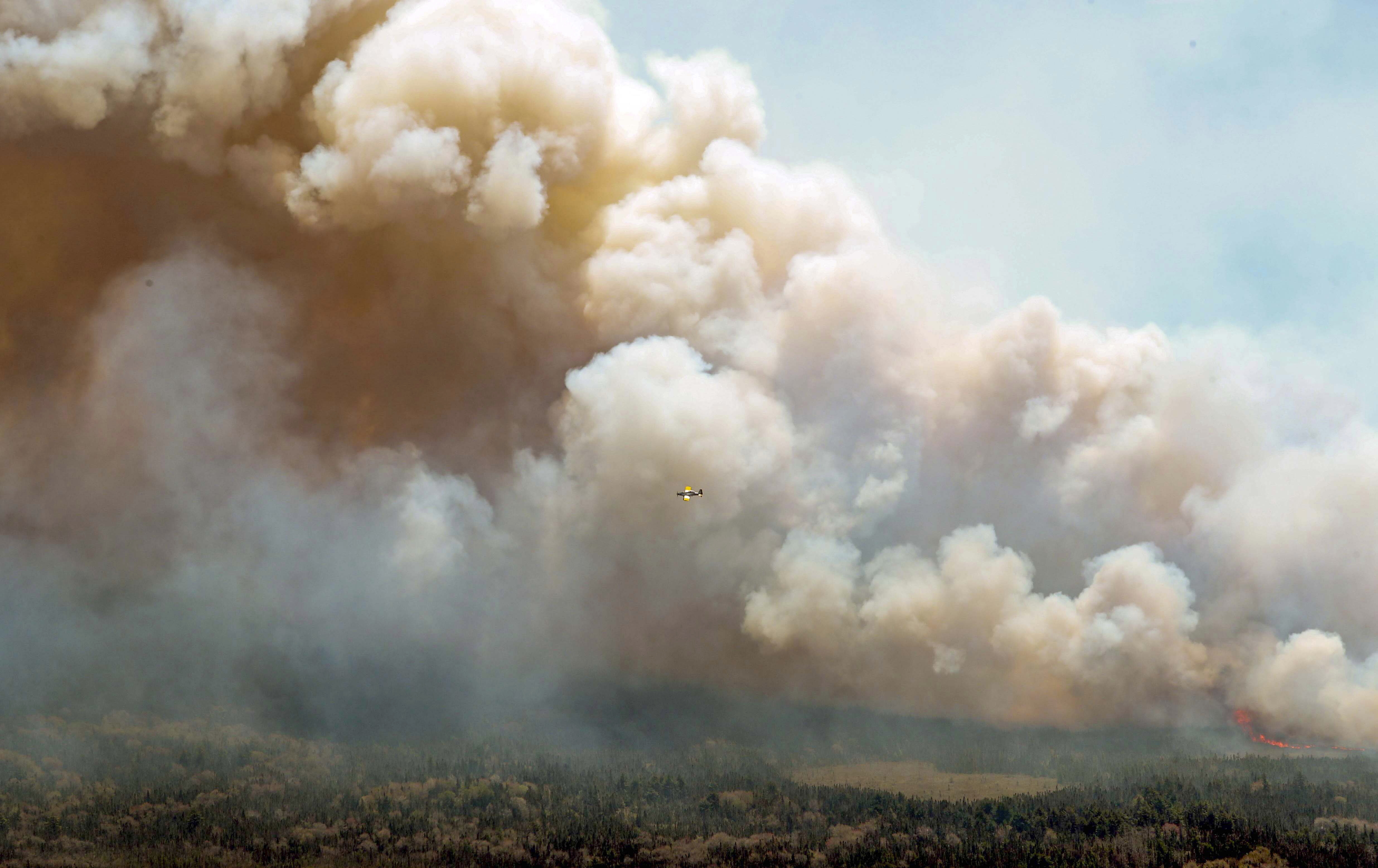 In this aerial image, an aircraft, center, flies near a wildfire burning near Barrington Lake in Shelburne County, Nova Scotia, on Wednesday, May 31, 2023. (Communications Nova Scotia/The Canadian Press via AP)