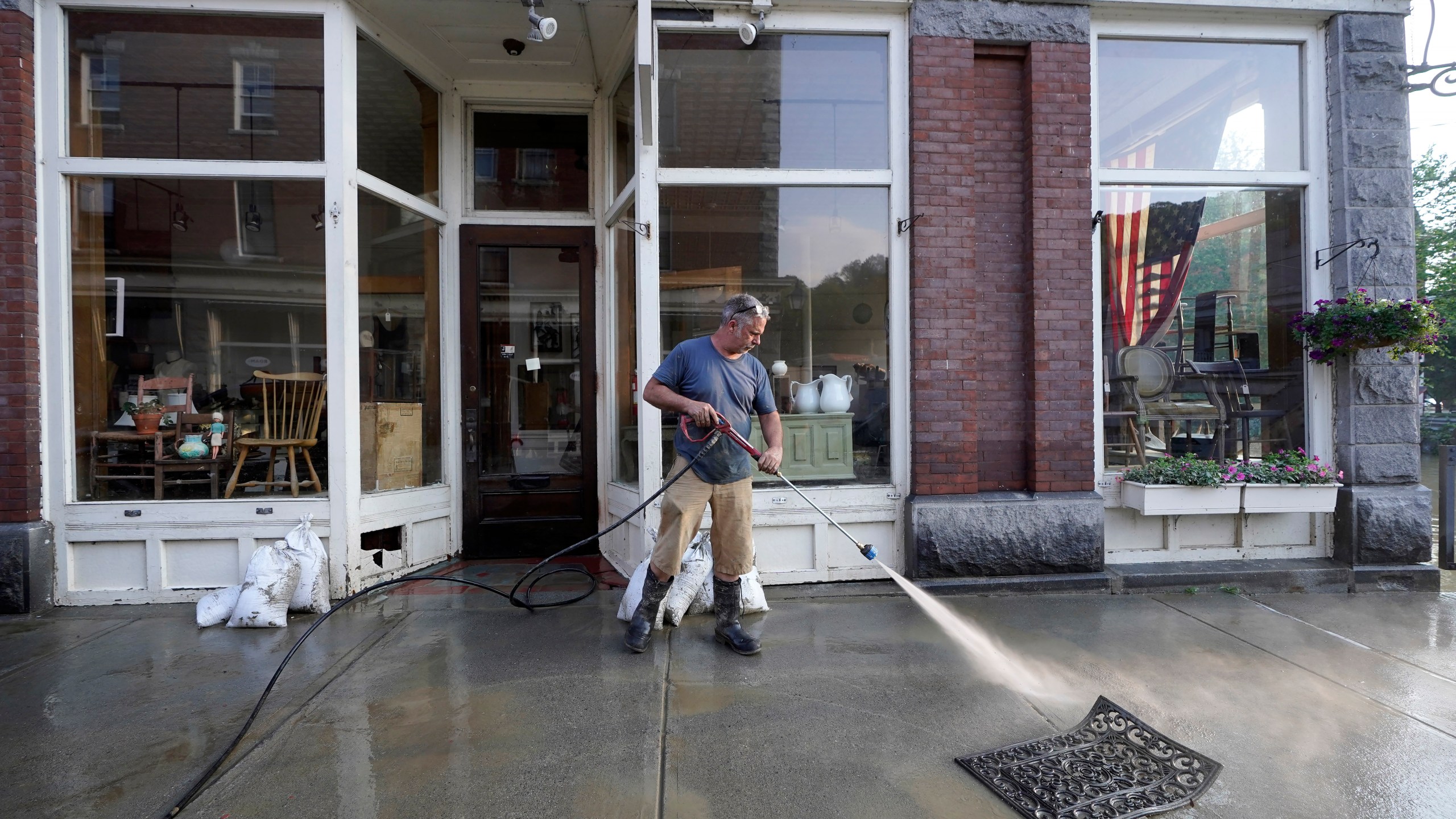 Simon Jennings, of Montpelier, Vt., washes the sidewalk in front of the flood-damaged antiques, art, and furnishings store he and his wife own in downtown Montpelier on Tuesday, July 11, 2023. A storm that dumped up ro two months of rain in two days brought more flooding across Vermont on Tuesday. (AP Photo/Steven Senne)