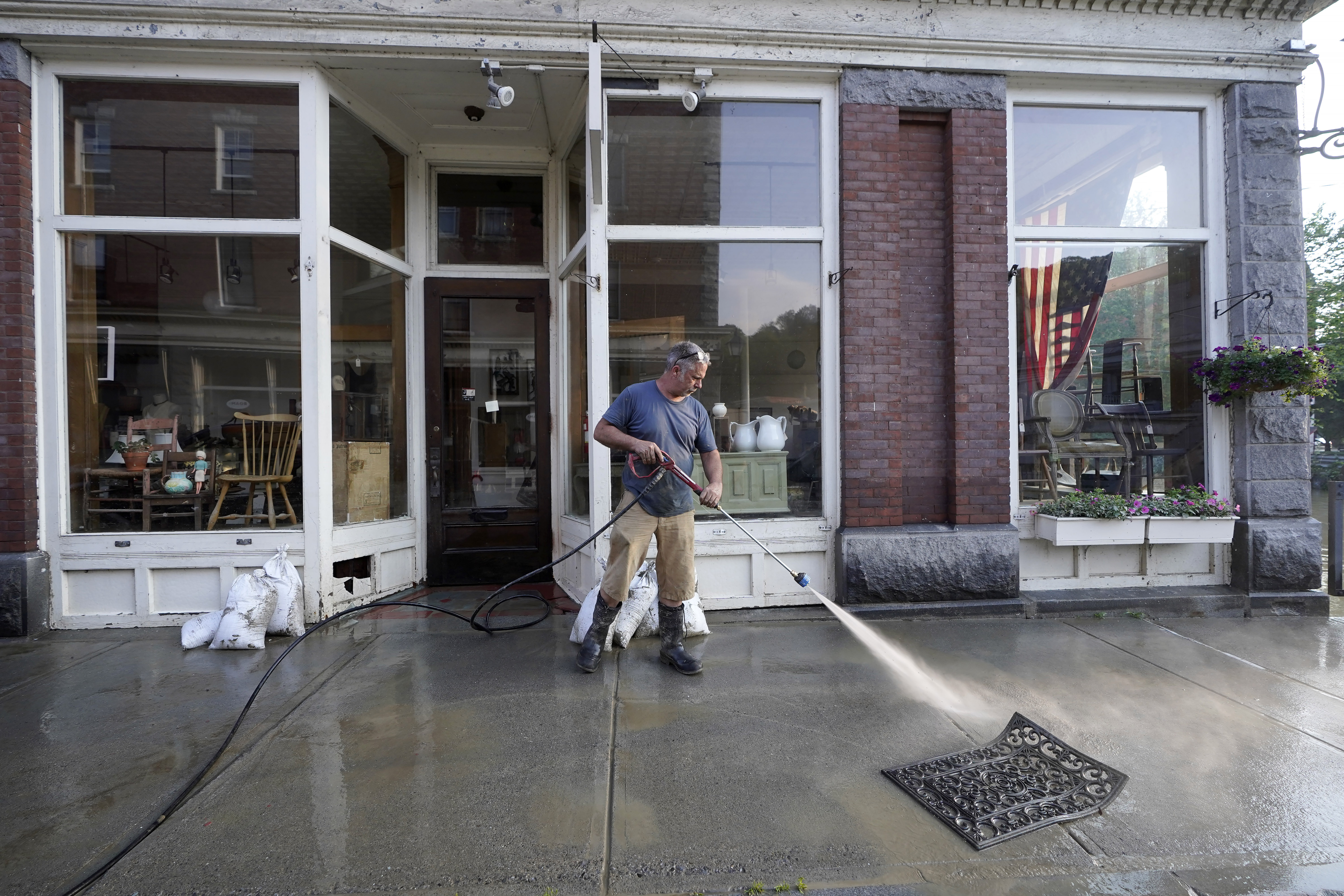 Simon Jennings, of Montpelier, Vt., washes the sidewalk in front of the flood-damaged antiques, art, and furnishings store he and his wife own in downtown Montpelier on Tuesday, July 11, 2023. A storm that dumped up ro two months of rain in two days brought more flooding across Vermont on Tuesday. (AP Photo/Steven Senne)