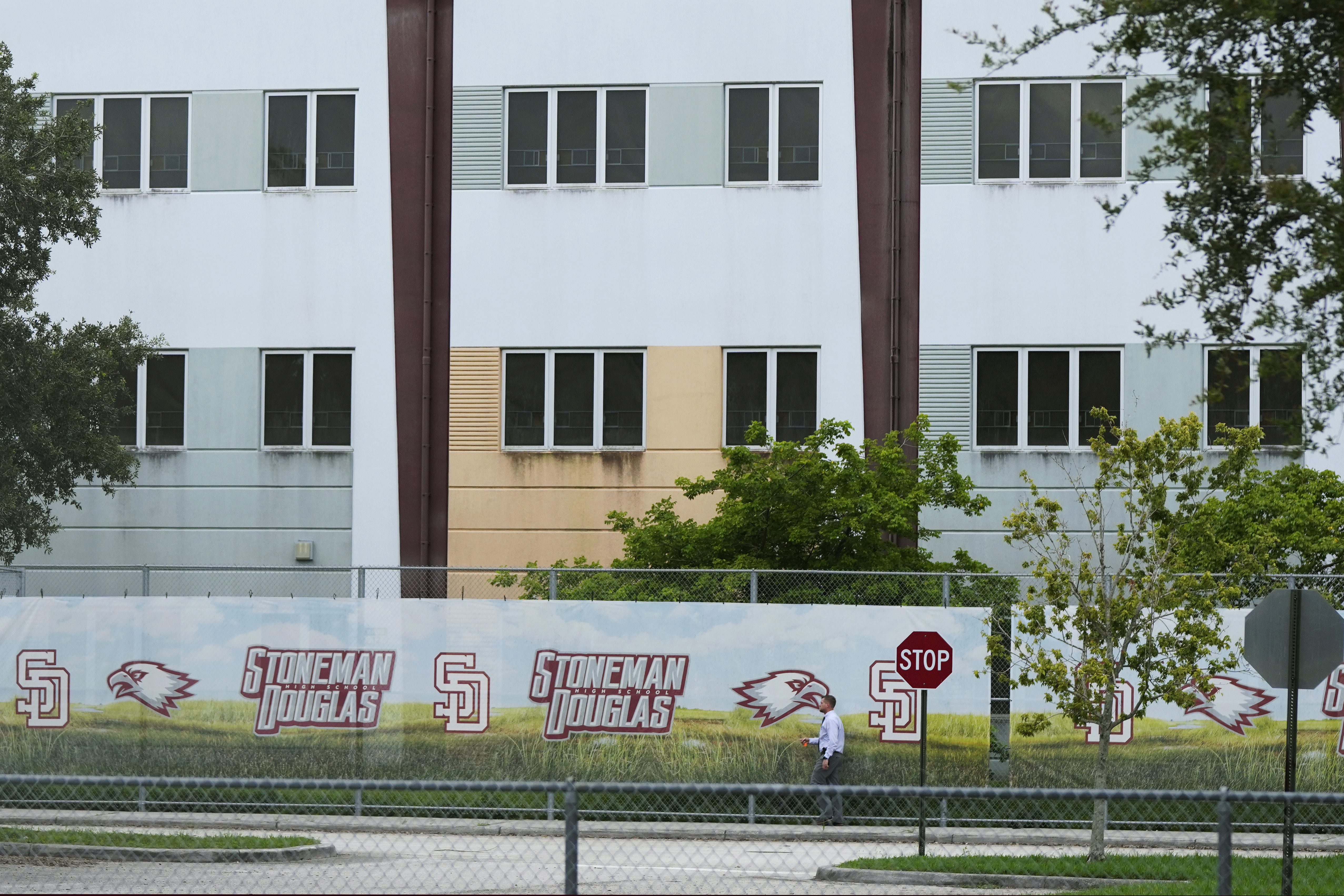 FILE - A security agent walks alongside a barrier surrounding Marjory Stoneman Douglas High School, July 5, 2023, in Parkland, Fla. Florida lawmakers and others on Saturday, Oct. 14, toured the school's 1200 Building, where a former student shot 17 people to death and wounded 17 others on Valentine's Day in 2018. The local school district has announced the 1200 Building will be demolished during the summer of 2024. (AP Photo/Rebecca Blackwell, File)