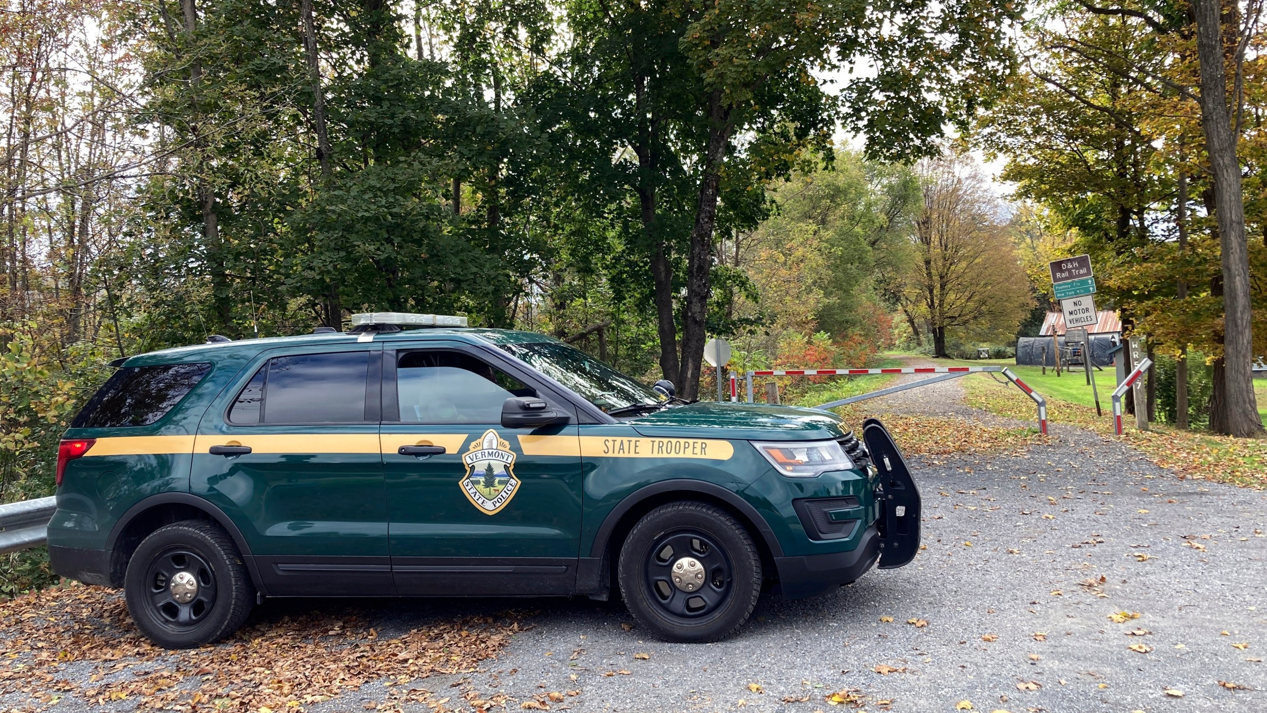 FILE - A Vermont State Police trooper sits parked in a cruiser on Oct. 11, 2023, at the entrance to a recreational trail in Castleton, Vt. Police are searching for the killer of a 77-year-old retired college dean who was shot while walking on the trail on Oct. 5. (AP Photo/Lisa Rathke, File)