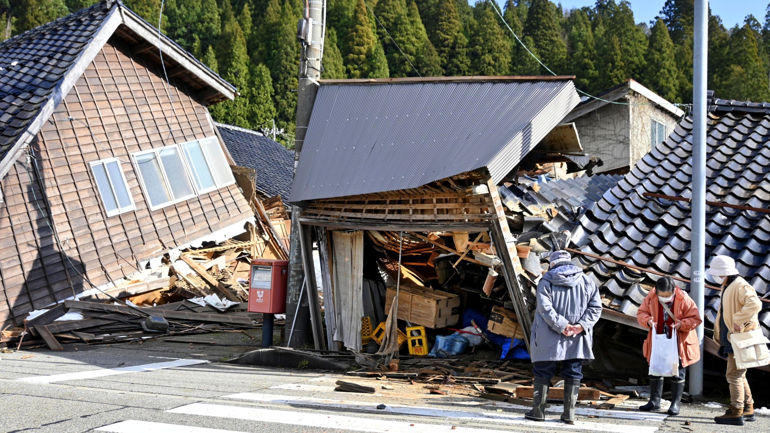 People look at collapsed buildings following earthquake in Wajima, Ishikawa prefecture, Japan Tuesday, Jan. 2, 2024. A series of powerful earthquakes in western Japan damaged homes, cars and boats, with officials warning people on Tuesday to stay away from their homes in some areas because of a continuing risk of major quakes and tsunamis. (Kyodo News via AP)