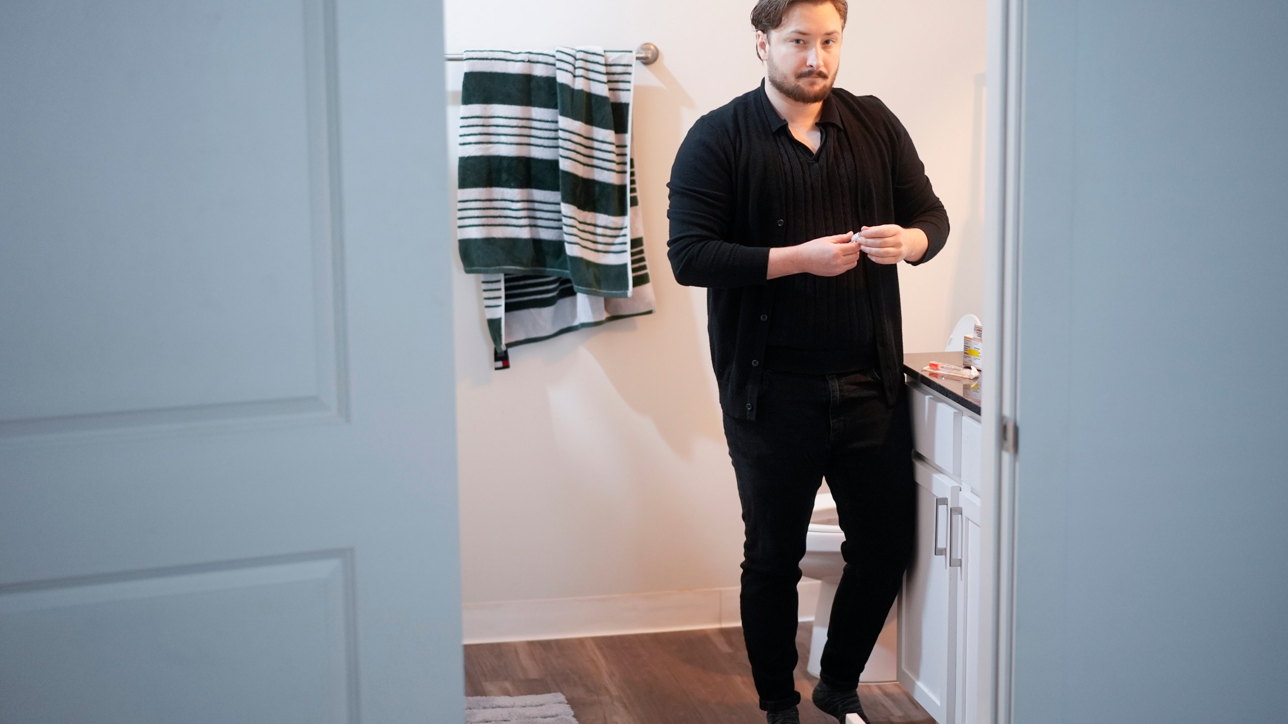 Ashton Colby holds a vial of Testosterone Cypionate Injection in his apartment bathroom in Columbus, Ohio, on Thursday, Jan. 18, 2024. Ohio Gov. Mike DeWine announced proposals this month that transgender advocates say could block access to gender-affirming care provided by independent clinics and general practitioners, leaving thousands of adults scrambling for treatment and facing health risks. Colby, 31, fears the clinic where he gets the testosterone he has taken since age 19 would no longer offer it. (AP Photo/Carolyn Kaster)