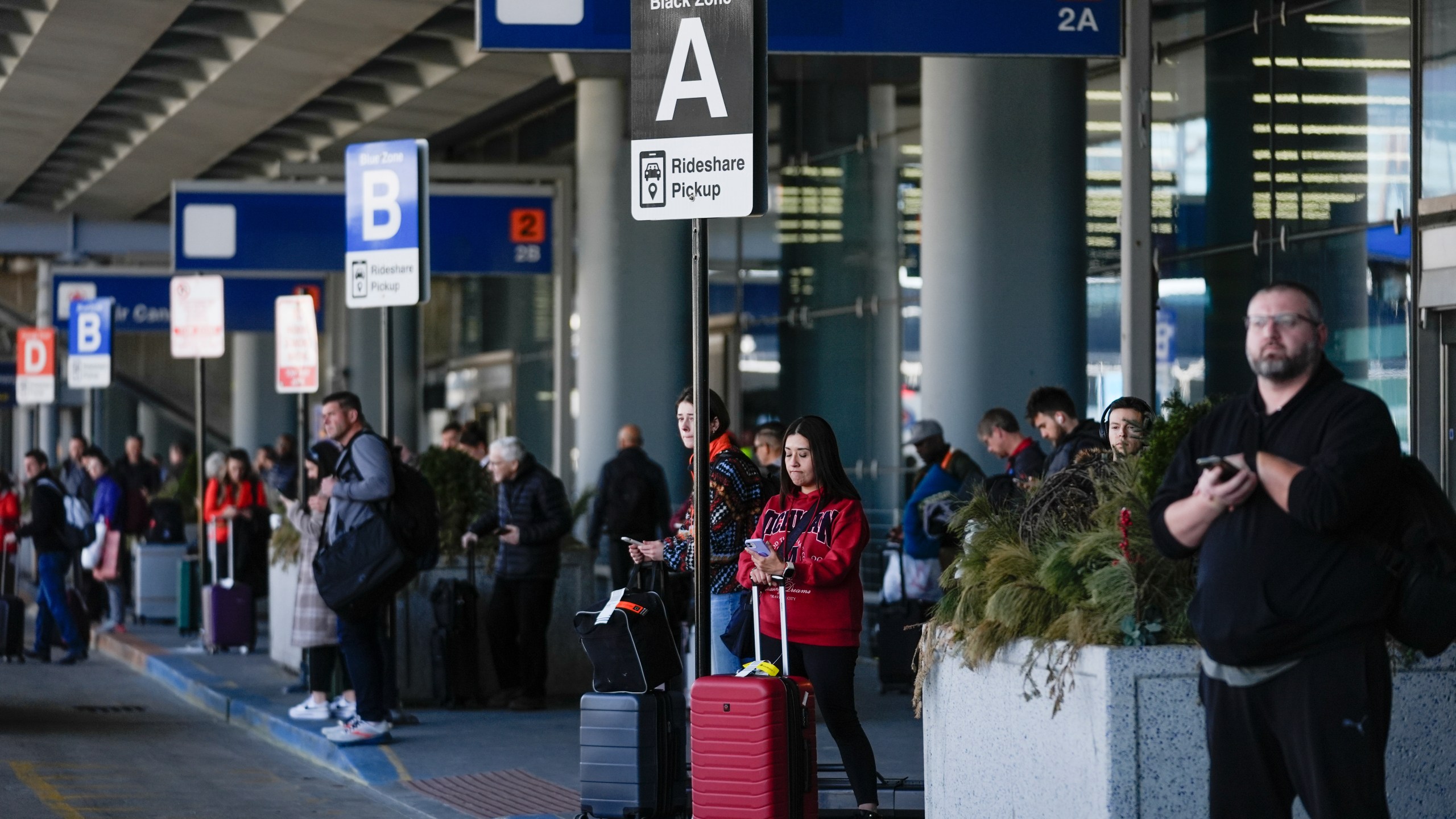 People wait in the rideshare pickup area at O'Hare International Airport, Wednesday, Feb. 14, 2024, in Chicago. Thousands of ride-hailing and delivery workers in the U.S. and the U.K. went on strike on Valentine's Day, calling for higher pay and other changes to their working conditions. (AP Photo/Erin Hooley)