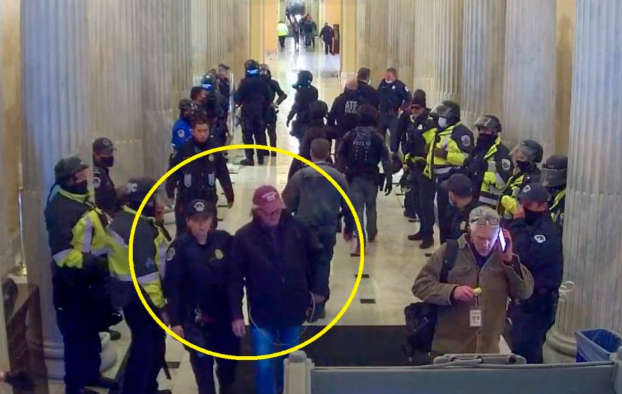 This image from U.S. Capitol Police video, contained and annotated in the Justice Department's statement of facts in support arrest warrant for Stephen Michael Baker, shows Baker, circled in yellow, being led from the U.S. Capitol on Jan. 6, 2021, in Washington, by a U.S. Capitol Police officer. Baker, a Texas-based writer for a conservative media outlet has surrendered to authorities to face charges that he joined a mob's attack on the U.S. Capitol on Jan. 6, 2021. (Department of Justice via AP)