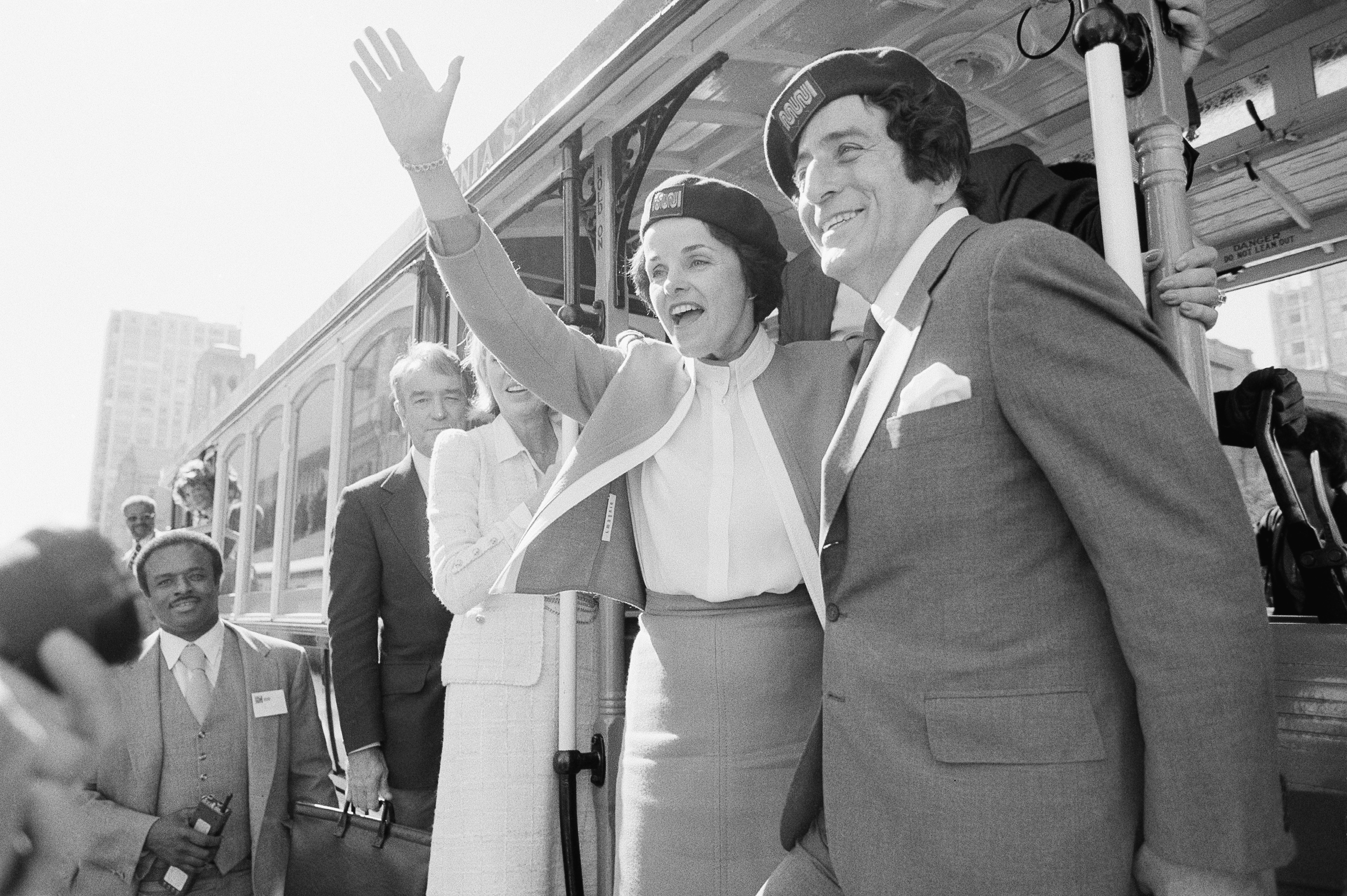 FILE - San Francisco Mayor Dianne Feinstein and singer Tony Bennett, who sang " I Left My Heart in San Francisco," hangs on to the outside of a cable car in San Francisco before taking a test ride, May 2, 1984. Bennett loved San Francisco and its cable cars and in return, the city has dedicated one of those cable cars to the famous crooner, who died in July 2023. Cable car 53, built in 1907, has several plaques and painted gold ribbons remembering Bennett. (AP Photo/Jeff Reinking, File)