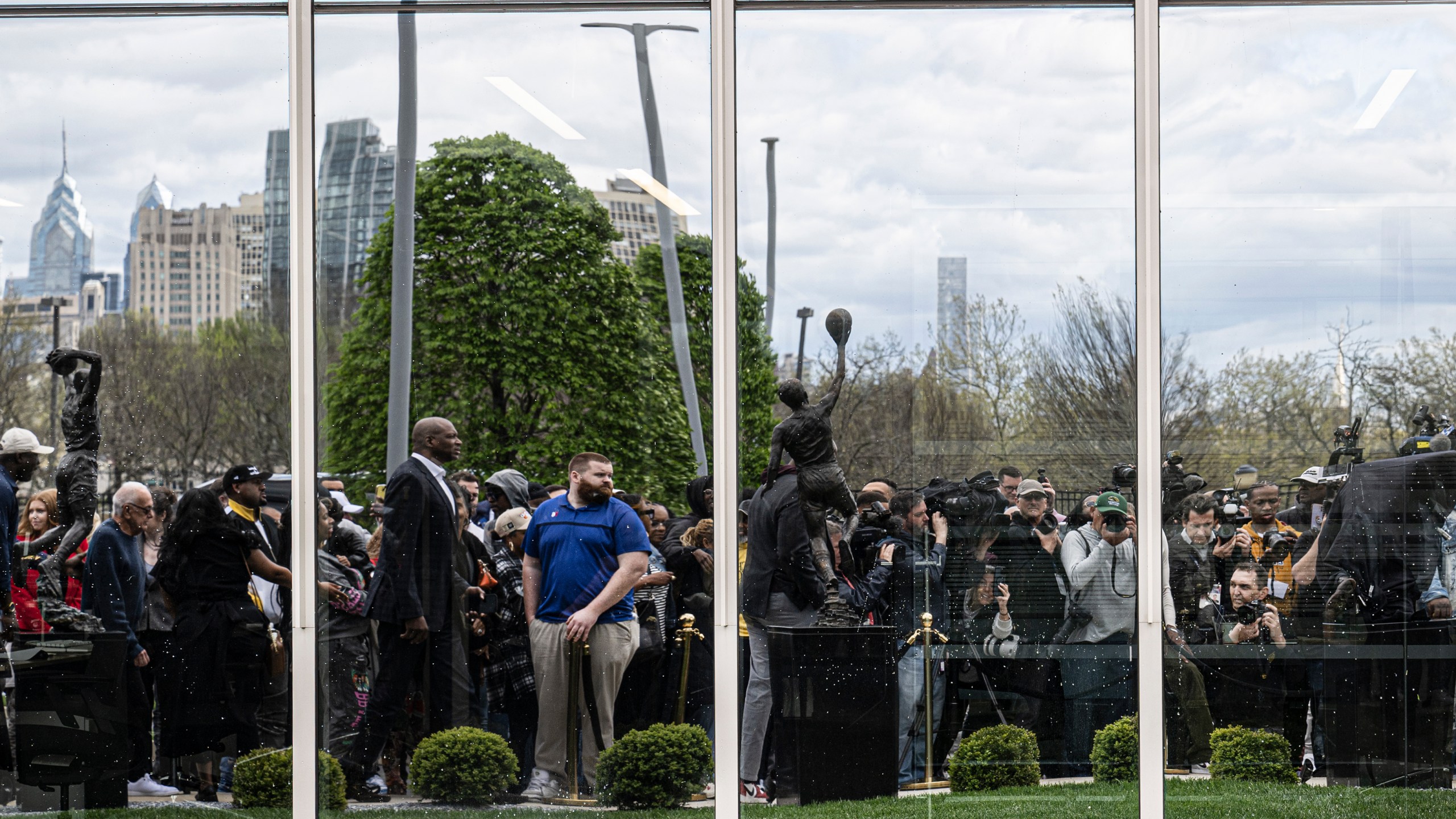 A larger crowd is reflected on a window during the unveiling of a statue of former Philadelphia 76ers NBA basketball player Allen Iverson, Friday, Apr 12, 2024, in Camden, N.J. (Jose F. Moreno/The Philadelphia Inquirer via AP)