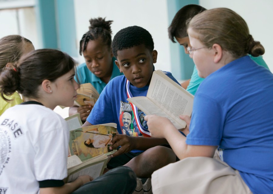 FILE - Joseph Webb, center; Kristina Carr, right; and Kaelyn Korovich, left, read outside their classroom at Air Base Elementary School, June 4, 2009, in Homestead, Fla. The school was one of the first in Miami-Dade County to integrate Black students. Friday, May 17, 2024, marks 70 years since the U.S. Supreme Court ruled that separating children in schools by race was unconstitutional. On paper, Brown v. Board of Education still stands. In reality, school integration is all but gone, the victim of a gradual series of court cases that slowly eroded it, leaving little behind. (AP Photo/Wilfredo Lee, File)