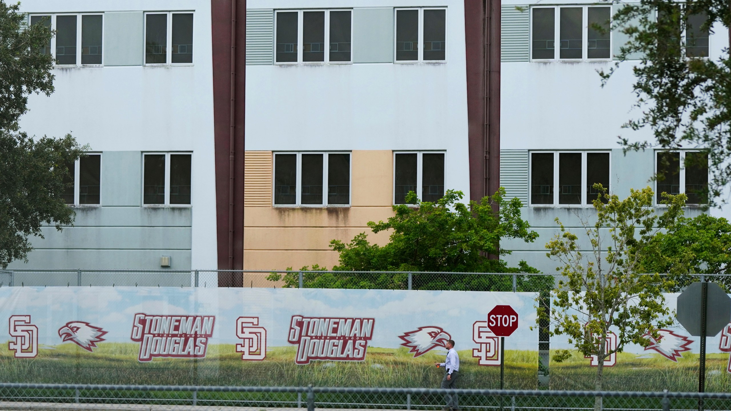 FILE - A security agent walks alongside a barrier surrounding Marjory Stoneman Douglas High School, July 5, 2023, in Parkland, Fla. Demolition of the building where 17 people died in the 2018 Parkland school shooting is set to begin, as crews will begin tearing down the three-story building at the high school on Thursday, June 13, 2024. (AP Photo/Rebecca Blackwell, File)