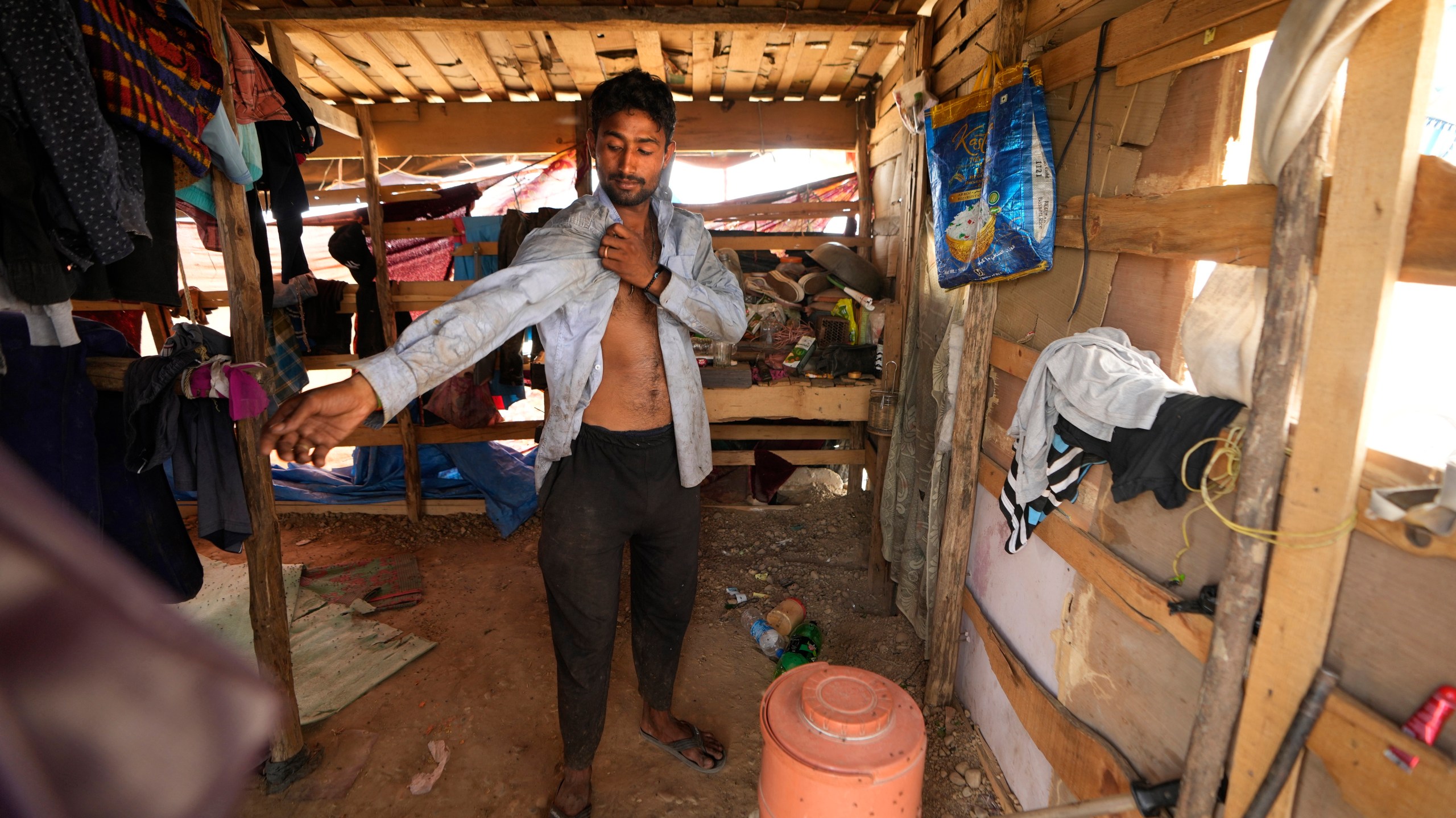 Aamir Shekh puts on a shirt before heading out in a heat wave to a garbage dump on the outskirts of Jammu, India, Wednesday, June 19, 2024. Shekh and his family are among millions of people who scratch out a living searching through India's waste — and climate change is making a hazardous job more dangerous than ever. (AP Photo/Channi Anand)