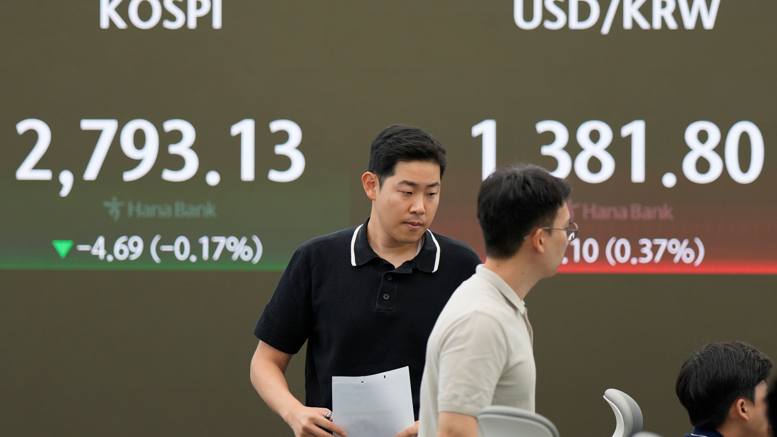 Currency traders walk by the screen showing the Korea Composite Stock Price Index (KOSPI), left, and the foreign exchange rate between U.S. dollar and South Korean won at a foreign exchange dealing room in Seoul, South Korea, Monday, July 1, 2024. (AP Photo/Lee Jin-man)