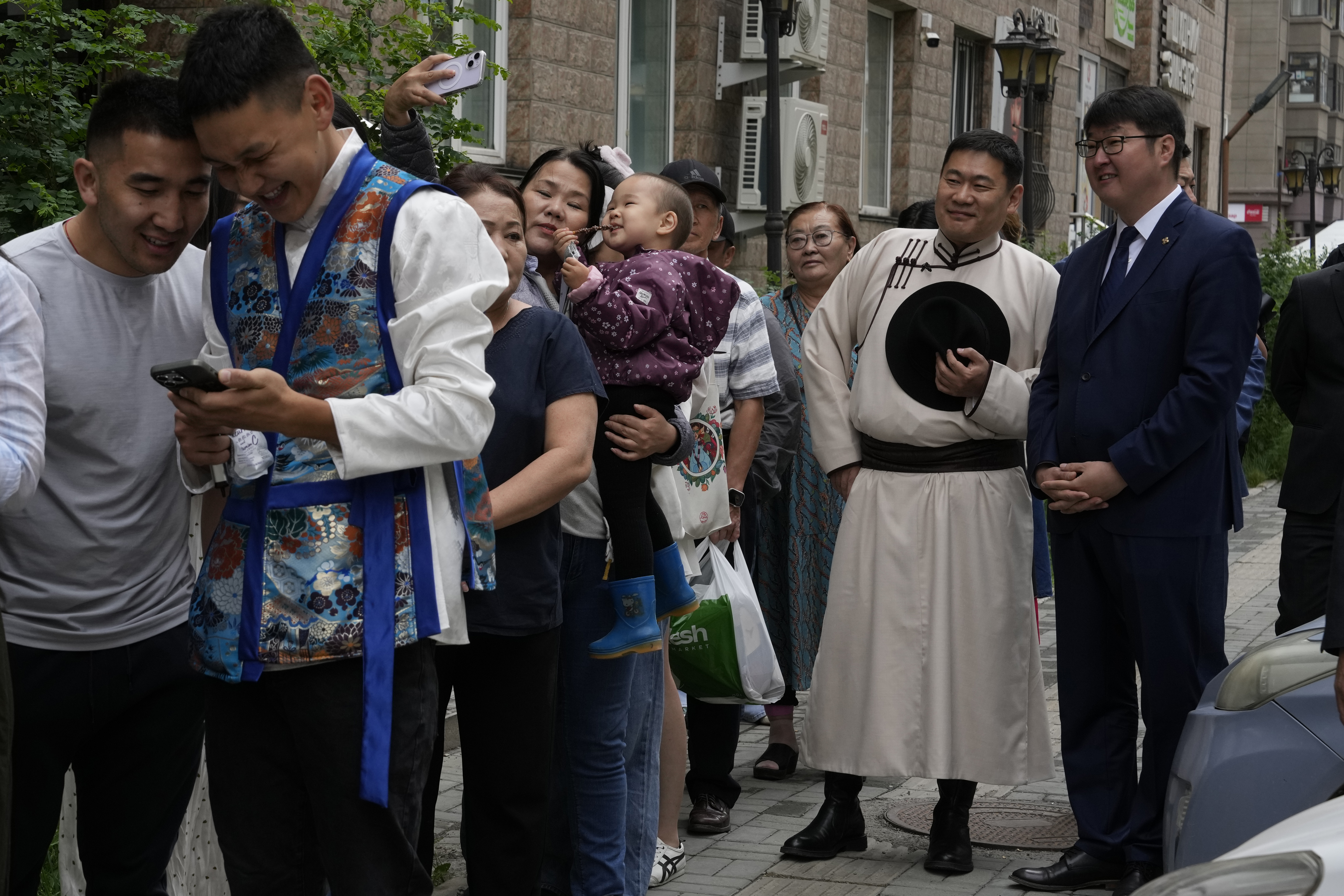 FILE - Mongolian Prime Minister Oyun-Erdene Luvsannamsrai, second from right, dressed in Mongolian traditional garment call deel, reacts as a woman takes a selfie with her child as he waited in line outside a polling station to vote in Ulaanbataar, Mongolia, June 28, 2024. The ruling People's Party has tried to reposition itself in response to the public discontent. It appointed the relatively young prime minister, Oyun-Erdene Luvsannamsrai, now 44, with a master's degree from Harvard University in 2021. (AP Photo/Ng Han Guan, File)