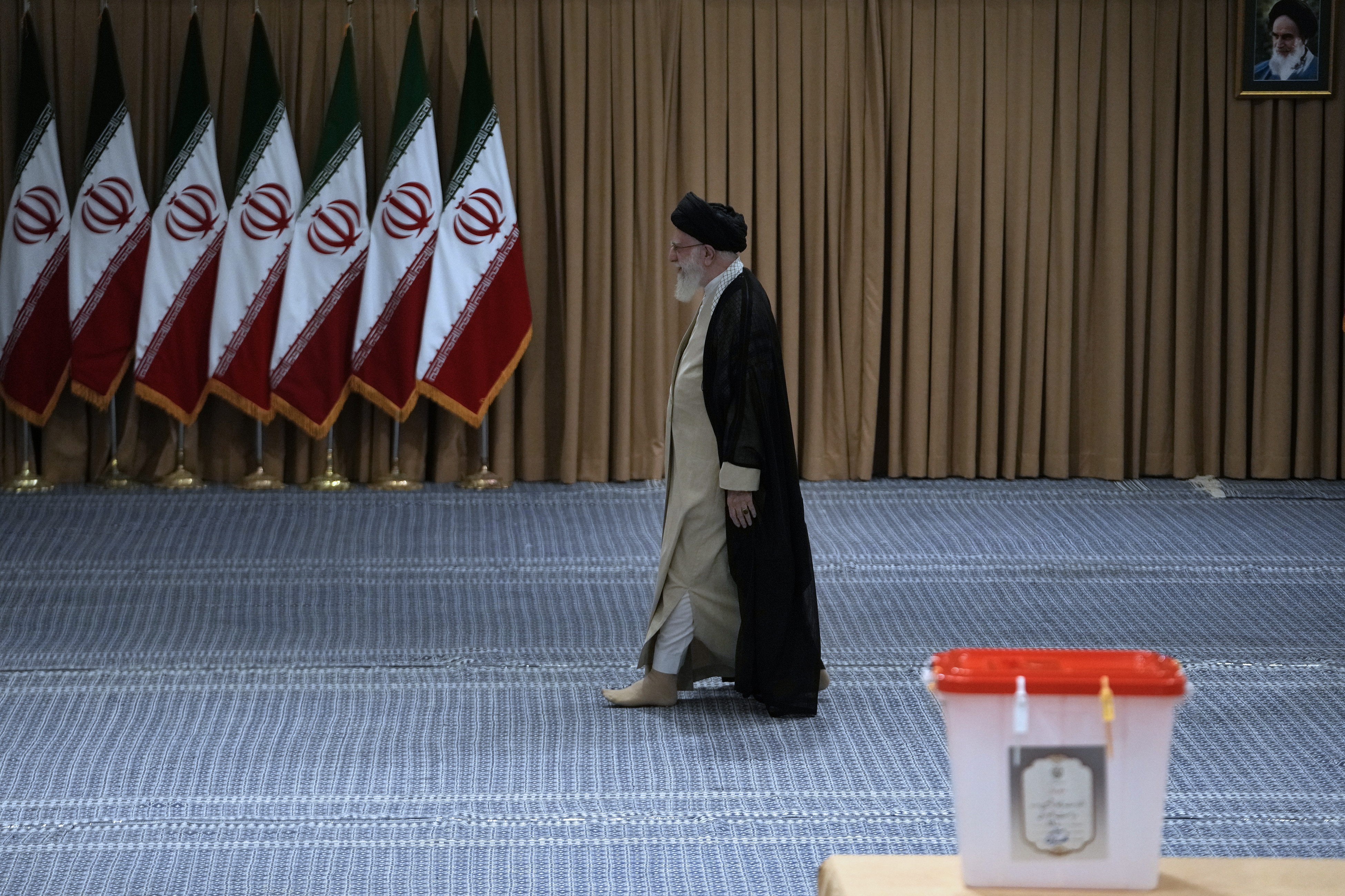 Iranian Supreme Leader Ayatollah Ali Khamenei arrives to vote for the presidential runoff election in Tehran, Iran, Friday, July 5, 2024. Iranians began voting Friday in a runoff election to replace the late President Ebrahim Raisi, killed in a helicopter crash last month, as public apathy has become pervasive in the Islamic Republic after years of economic woes, mass protests and tensions in the Middle East. A picture of the late revolutionary founder Ayatollah Khomeini hangs on top right. (AP Photo/Vahid Salemi)