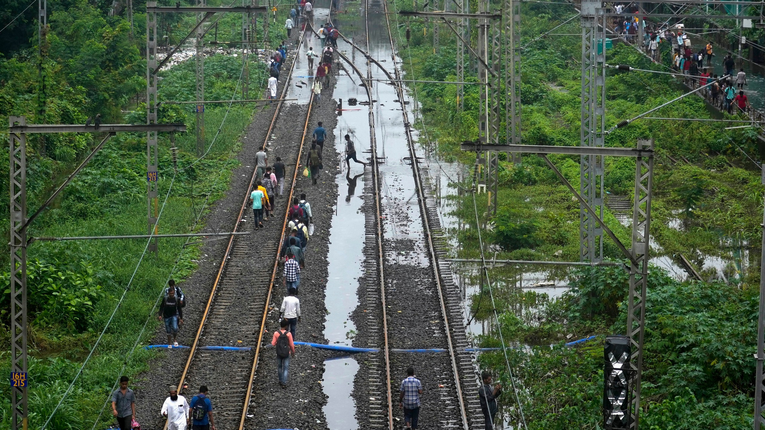 Commuters walk on railway tracks after trains were disrupted due to heavy rainfall in Mumbai, India, Monday, July 8, 2024. (AP Photo/Rafiq Maqbool)