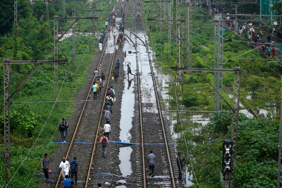 Commuters walk on railway tracks after trains were disrupted due to heavy rainfall in Mumbai, India, Monday, July 8, 2024. (AP Photo/Rafiq Maqbool)