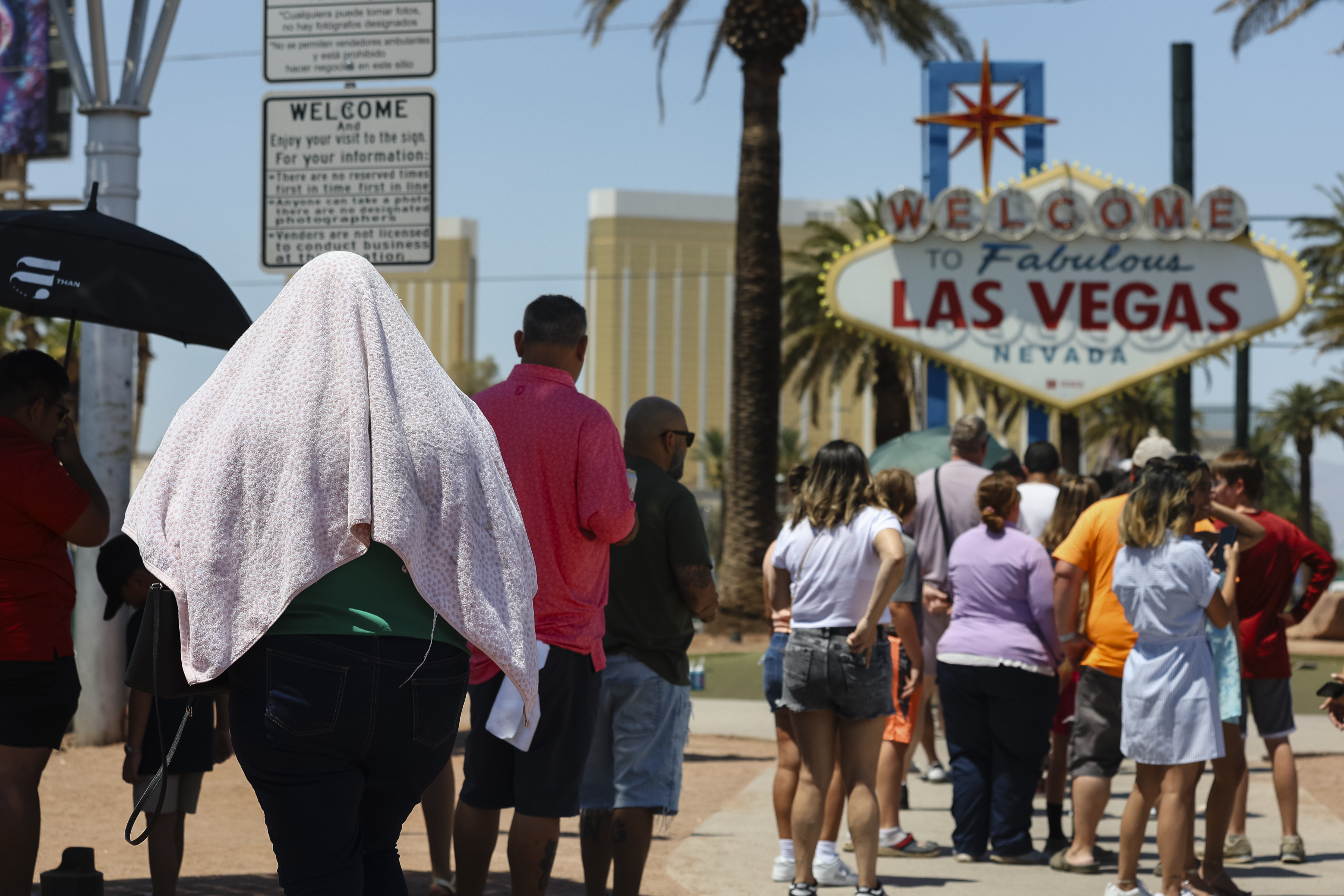 A person uses a blanket to block the sun while waiting to take a photo at the "Welcome to Las Vegas" sign Monday, July 8, 2024, in Las Vegas. After causing deaths and shattering records in the West over the weekend, a long-running heat wave will again grip the U.S. on Monday, with hot temperatures also predicted for large parts of the East Coast and the South. (Wade Vandervort/Las Vegas Sun via AP)