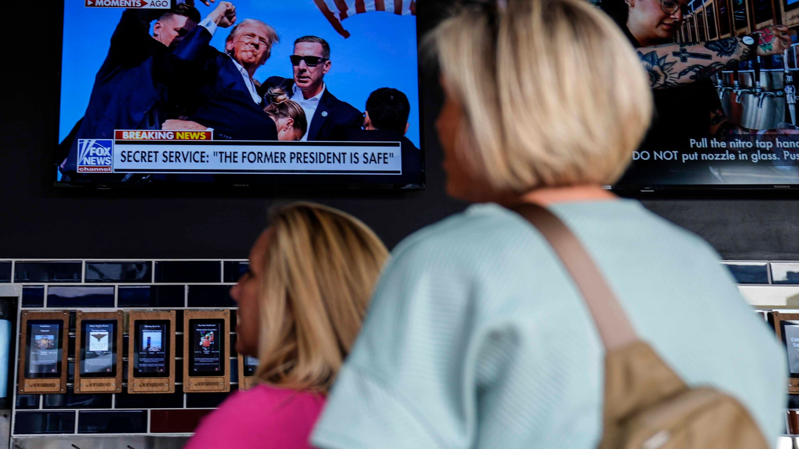 People watch news near the Fiserv Forum ahead of the 2024 Republican National Convention, Saturday, July 13, 2024, in Milwaukee. Former president Donald Trump was whisked off the stage at a rally in Butler, Pennsylvania after apparent gunshots rang through the crowd.(AP Photo/Matt Rourke)