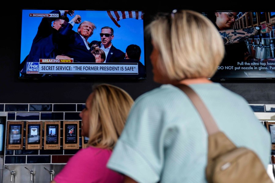 People watch news near the Fiserv Forum ahead of the 2024 Republican National Convention, Saturday, July 13, 2024, in Milwaukee. Former president Donald Trump was whisked off the stage at a rally in Butler, Pennsylvania after apparent gunshots rang through the crowd.(AP Photo/Matt Rourke)