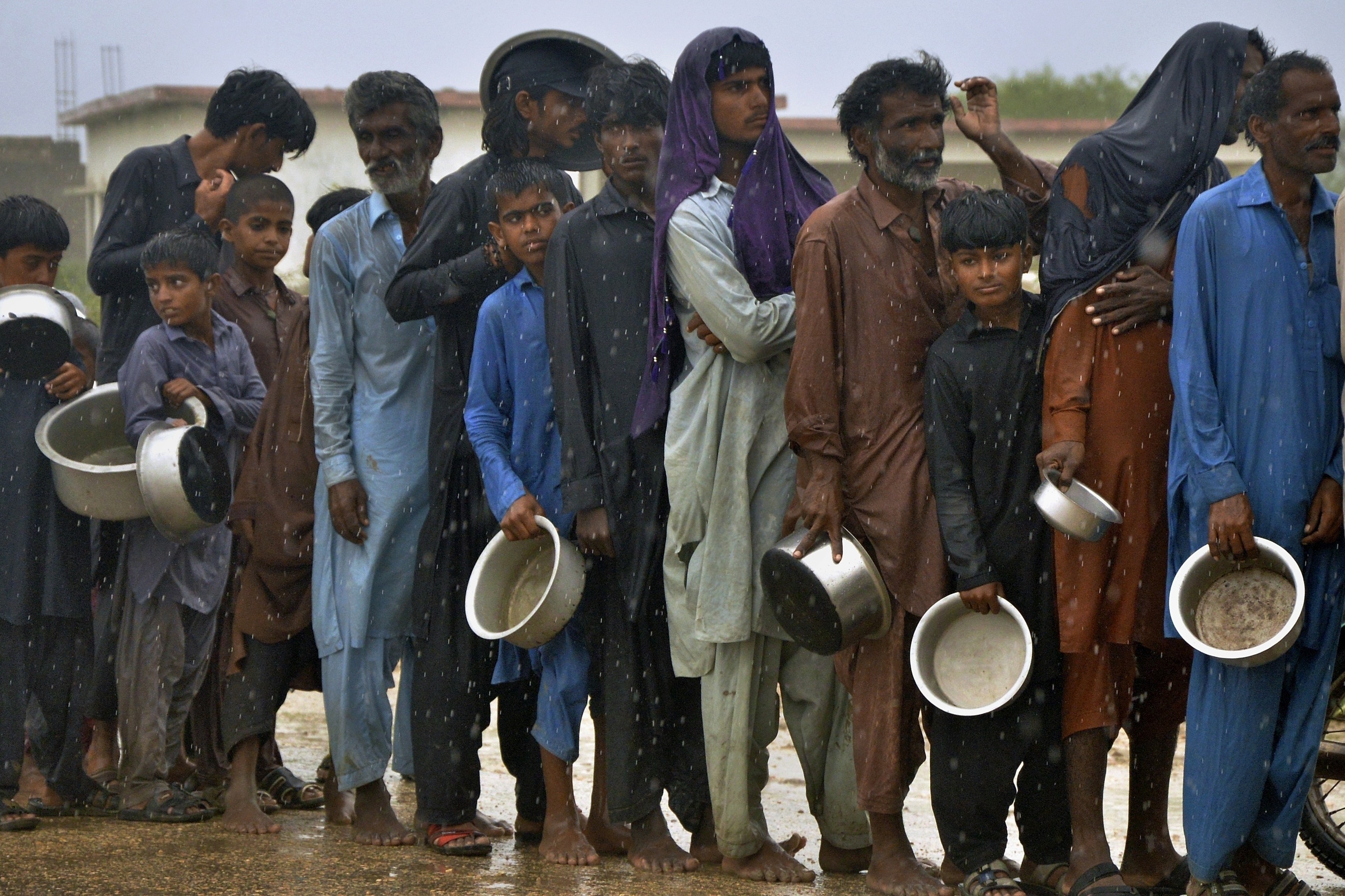 FILE - People wait in the rain to receive free food distributed from volunteers outside a camp for people displaced from coastal areas in Sujawal, Pakistan's southern district in the Sindh province, June 15, 2023, as Cyclone Biparjoy was approaching. (AP Photo/Pervez Masih, File)