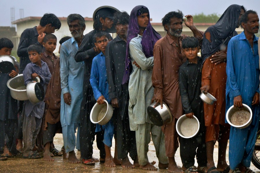 FILE - People wait in the rain to receive free food distributed from volunteers outside a camp for people displaced from coastal areas in Sujawal, Pakistan's southern district in the Sindh province, June 15, 2023, as Cyclone Biparjoy was approaching. (AP Photo/Pervez Masih, File)