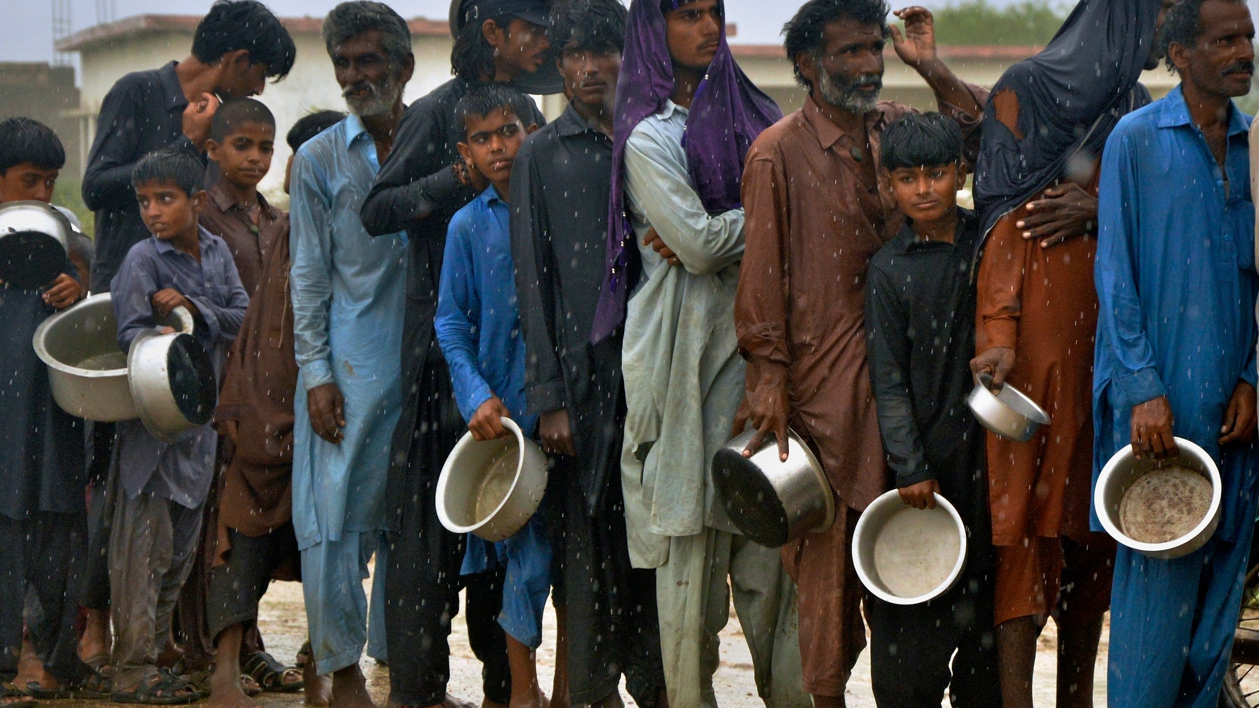 FILE - People wait in the rain to receive free food distributed from volunteers outside a camp for people displaced from coastal areas in Sujawal, Pakistan's southern district in the Sindh province, June 15, 2023, as Cyclone Biparjoy was approaching. (AP Photo/Pervez Masih, File)