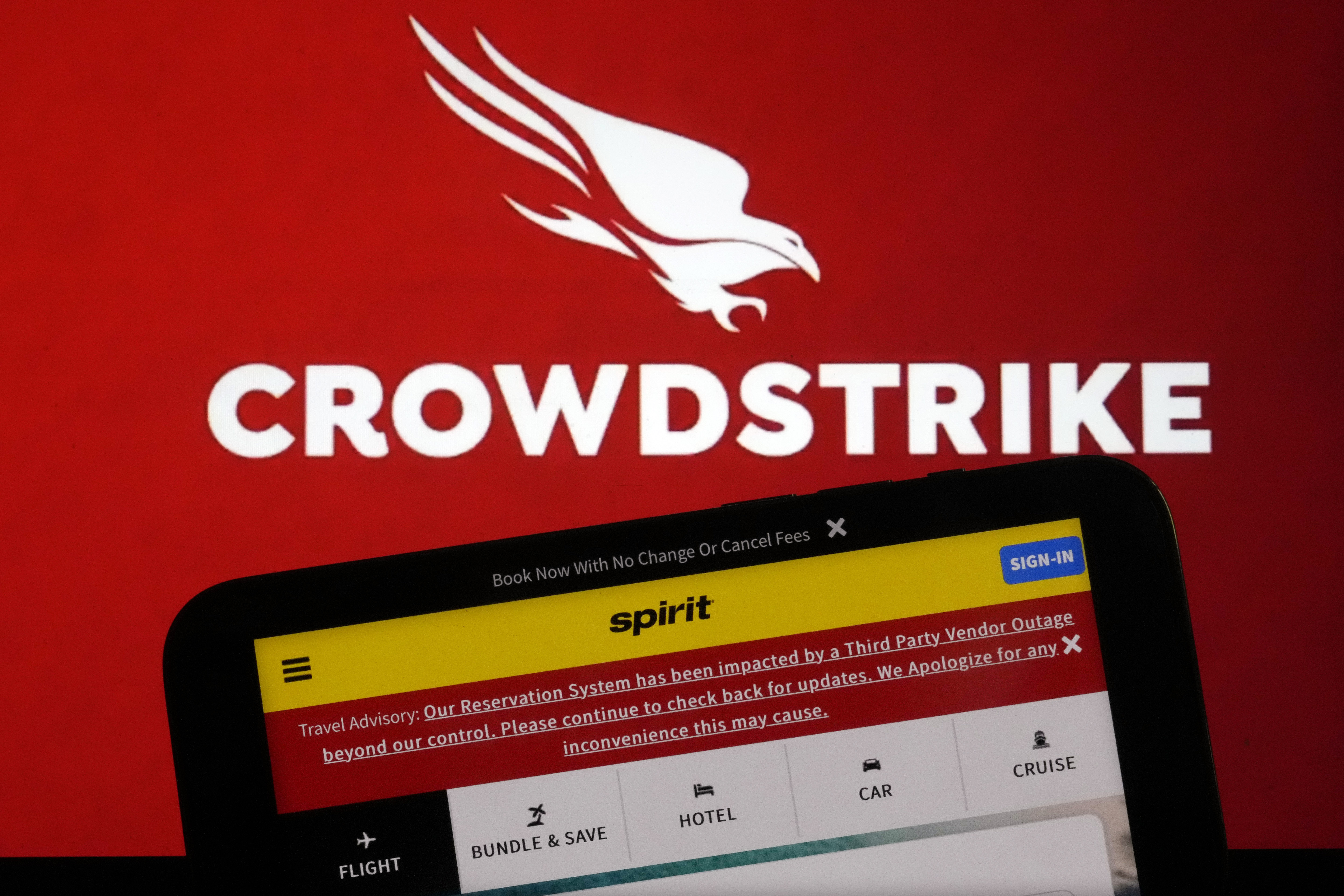 The logo for CrowdStrike and a Spirit Airlines webpage are shown on a computer screen and mobile phone screen, in New York, Friday, July 19, 2024. A global technology outage grounded flights, knocked banks offline and media outlets off air after a faulty software update disrupted companies and services around the world and highlighted their dependence on just a handful of providers. (AP Photo/Richard Drew)
