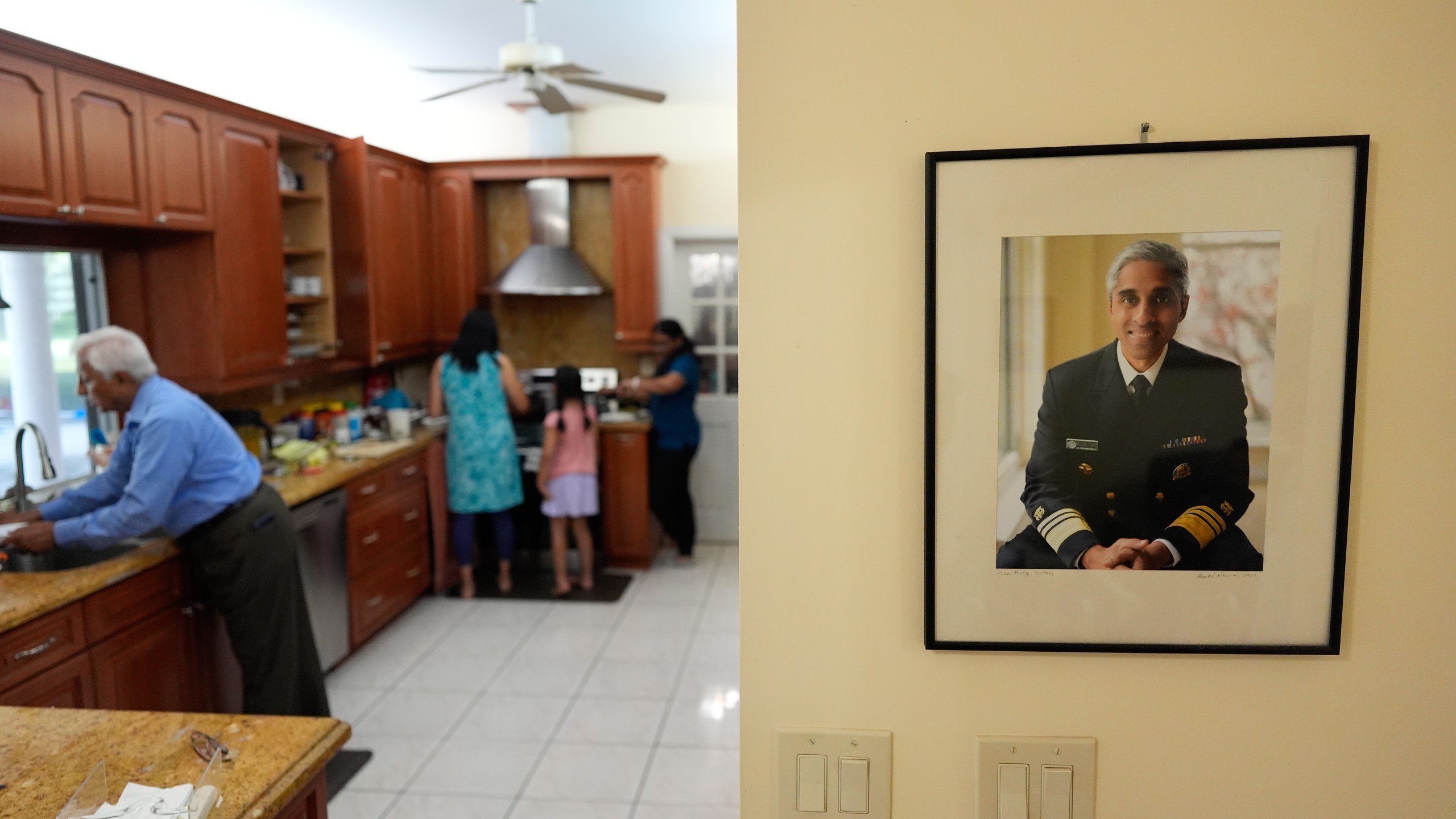 An official portrait of Surgeon General Dr. Vivek Murthy hangs on the wall of his parents' home, as family members make dinner, Tuesday, July 16, 2024, near Miami, Fla. (AP Photo/Rebecca Blackwell)