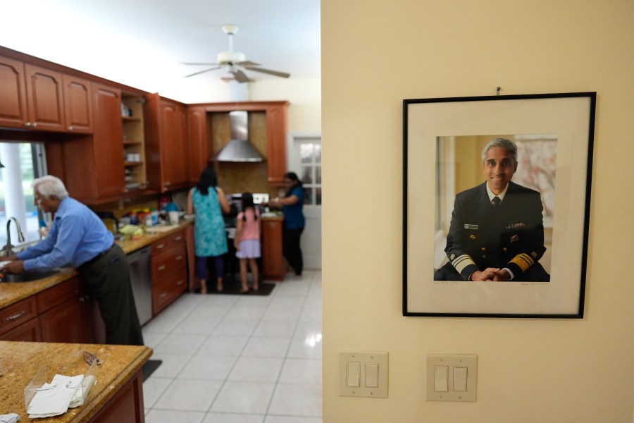 An official portrait of Surgeon General Dr. Vivek Murthy hangs on the wall of his parents' home, as family members make dinner, Tuesday, July 16, 2024, near Miami, Fla. (AP Photo/Rebecca Blackwell)