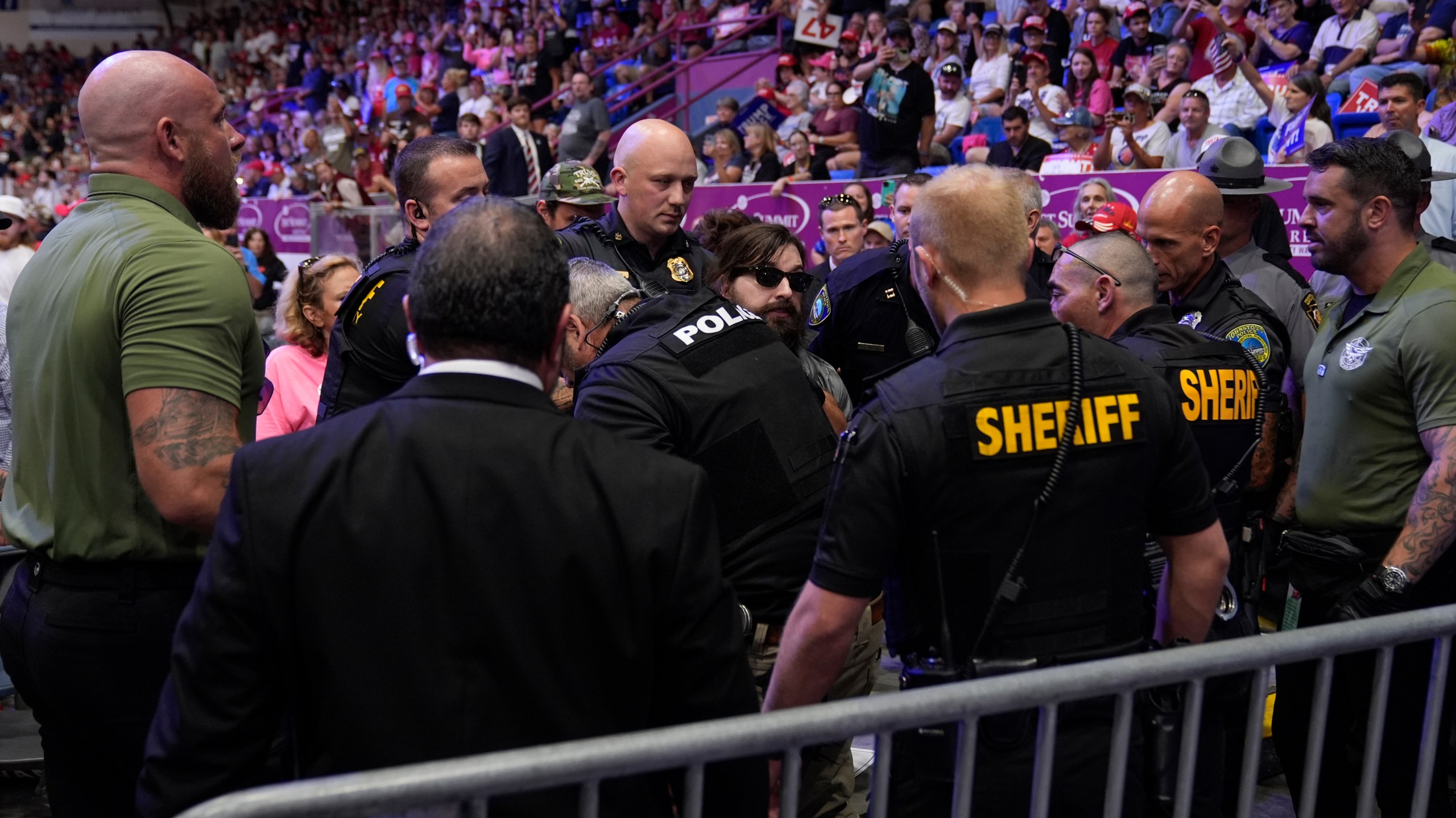 Police remove a man, center with sunglasses, who had climbed onto the media riser, as Republican presidential nominee former President Donald Trump speaks at a campaign event, Friday, Aug. 30, 2024, in Johnstown, Pa. (AP Photo/Alex Brandon)