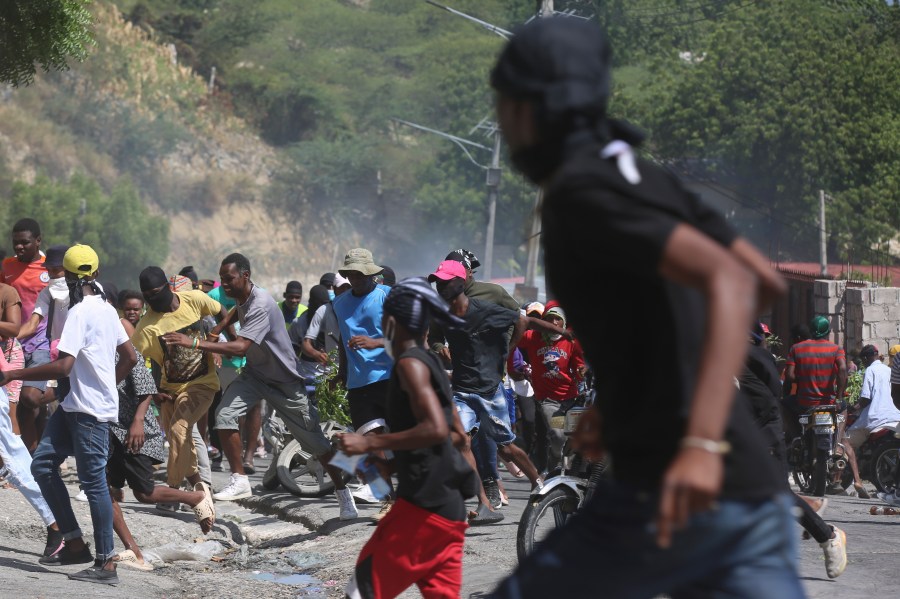 People run from tear gas fired by police to disperse protesters demanding police and the Prime Minister take immediate action against gangs in Port-au-Prince, Haiti, Monday, Aug. 19, 2024. (AP Photo/Odelyn Joseph)