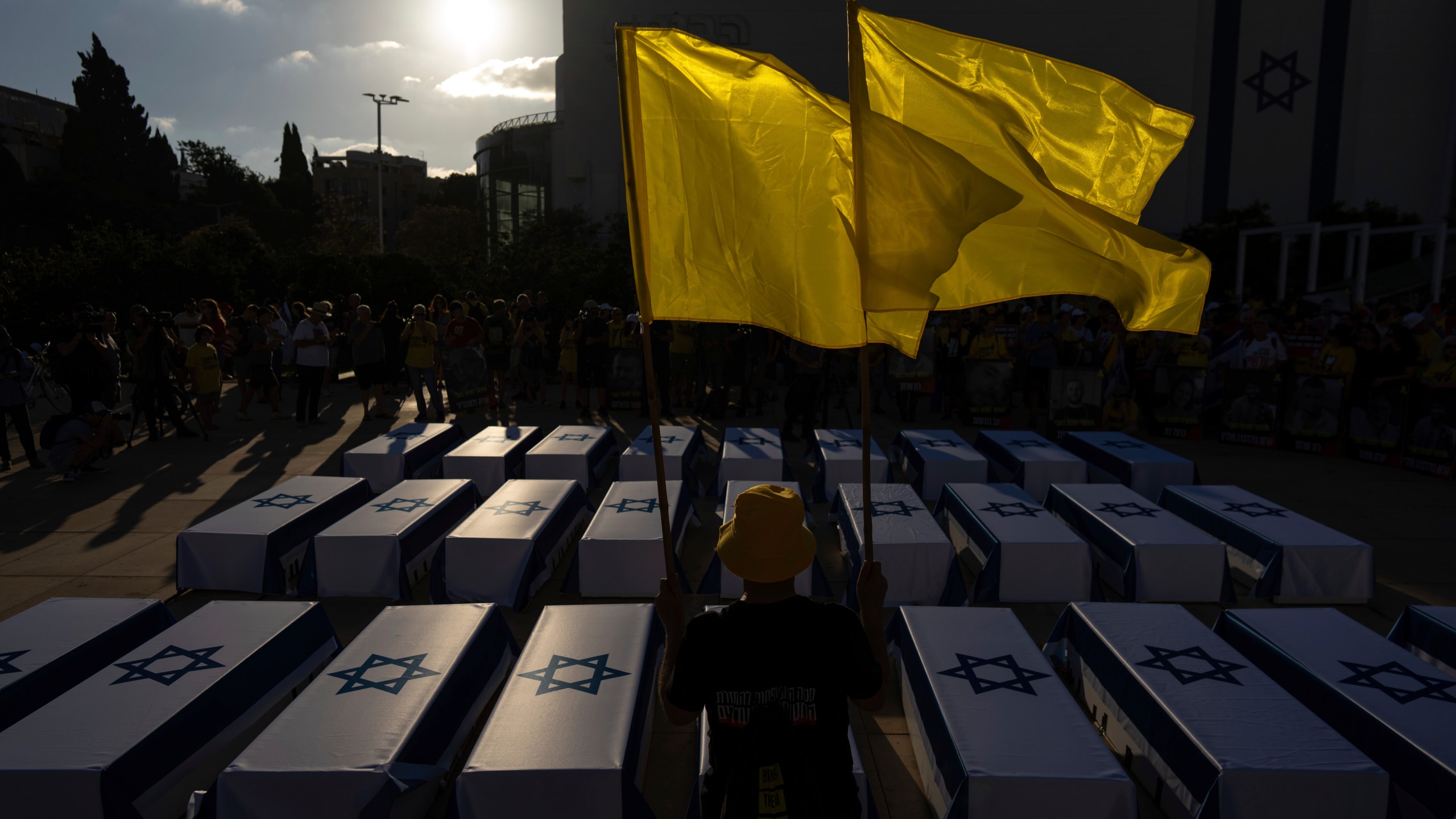 A man holds flags next to mock coffins covered in Israeli flags representing the 27 hostages whose bodies have been recovered from Gaza, during a rally demanding a cease-fire deal and the immediate release of hostages held by Hamas in the Gaza Strip on Thursday, Sept. 5, 2024, in Tel Aviv, Israel. (AP Photo/Ohad Zwigenberg)