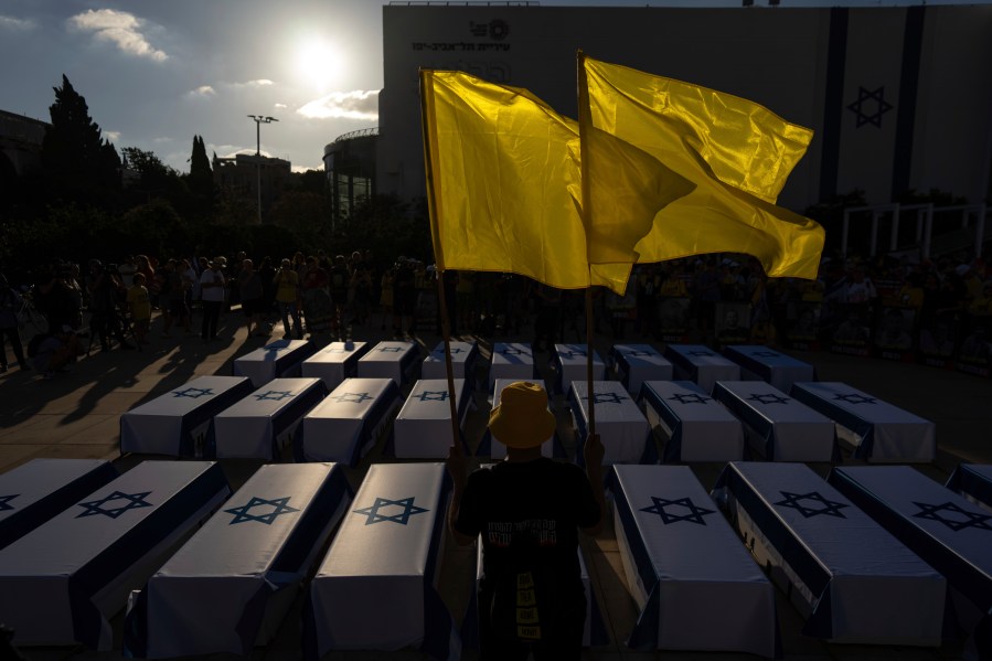 A man holds flags next to mock coffins covered in Israeli flags representing the 27 hostages whose bodies have been recovered from Gaza, during a rally demanding a cease-fire deal and the immediate release of hostages held by Hamas in the Gaza Strip on Thursday, Sept. 5, 2024, in Tel Aviv, Israel. (AP Photo/Ohad Zwigenberg)