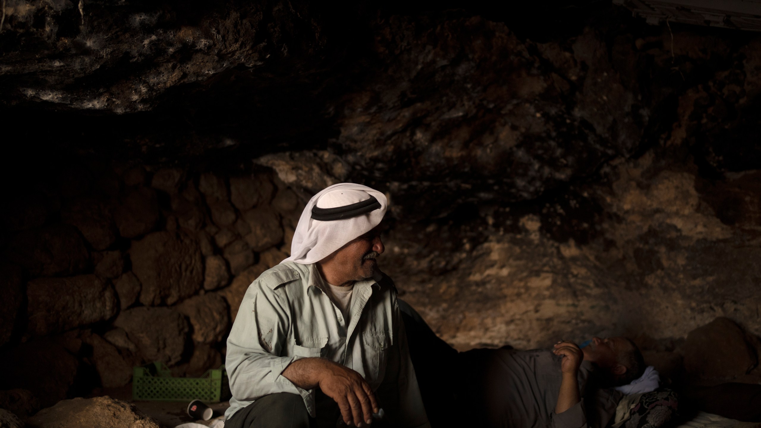 Palestinians Ribhi Ahmad Battat, left, and Issa Ahmad Battat, residents of the West Bank village of Khirbet Zanuta, take shelter from the midday sun in a cave Tuesday, Aug. 27, 2024. Ten months after settlers threatened to kill them if they didn't leave their village, some Palestinian residents are finally home, under a rare court order. (AP Photo/Maya Alleruzzo)