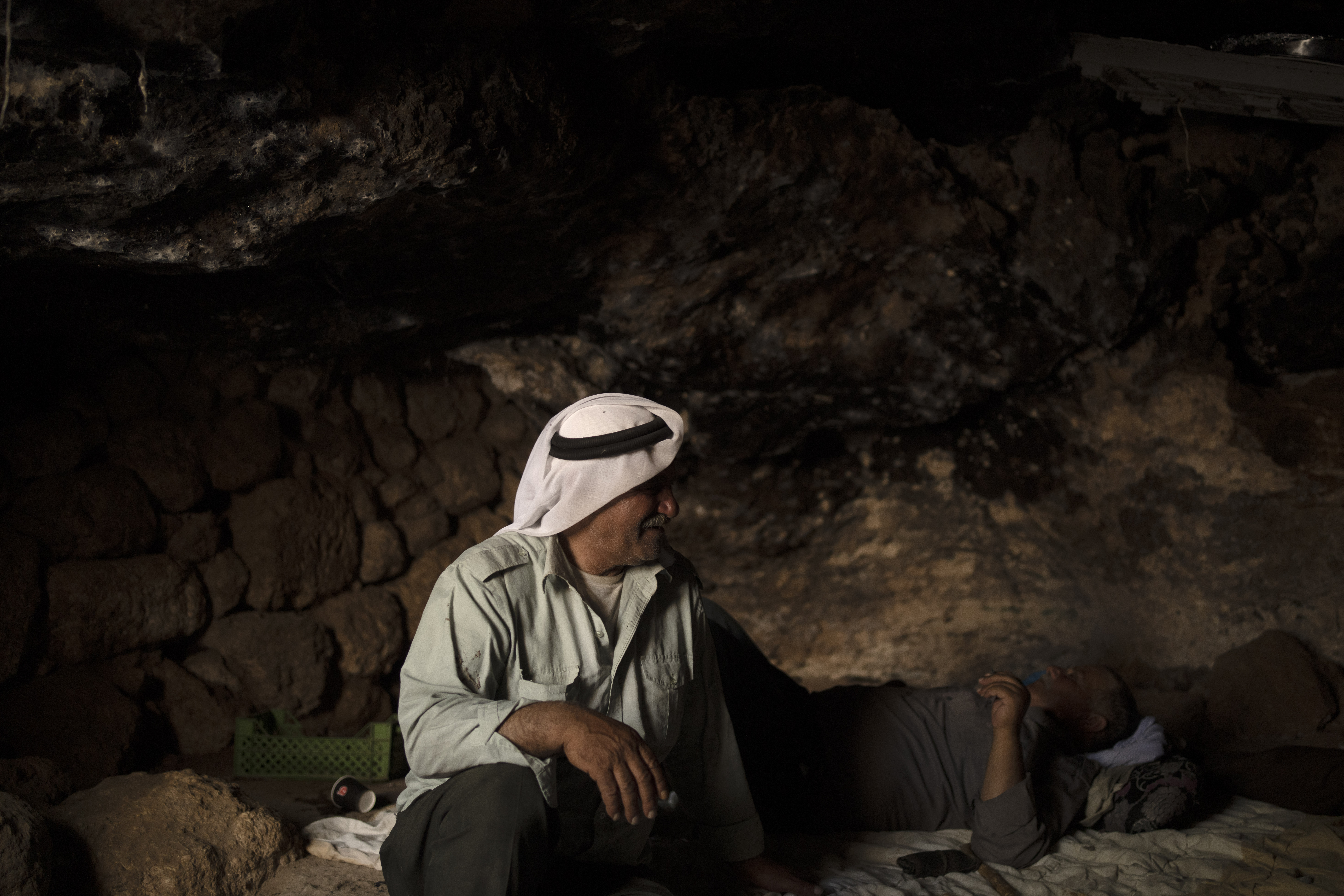 Palestinians Ribhi Ahmad Battat, left, and Issa Ahmad Battat, residents of the West Bank village of Khirbet Zanuta, take shelter from the midday sun in a cave Tuesday, Aug. 27, 2024. Ten months after settlers threatened to kill them if they didn't leave their village, some Palestinian residents are finally home, under a rare court order. (AP Photo/Maya Alleruzzo)