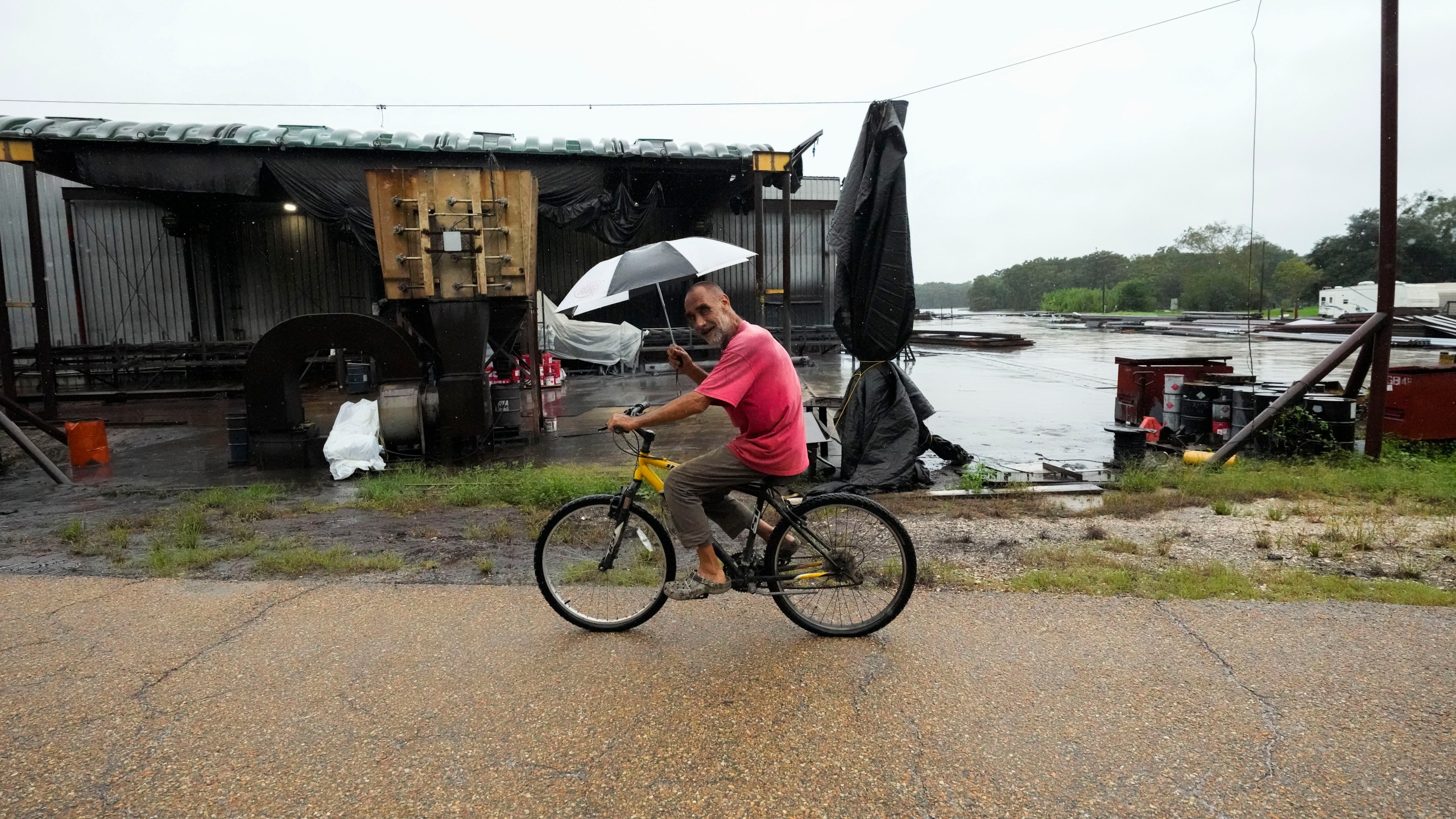 Kevin "Choupie" Badle, 67, rides his bike with an umbrella to buy more cigarettes at the store ahead of Hurricane Francine, expected to make landfall this evening, in Stephenville, La., Wednesday, Sept. 11, 2024. (AP Photo/Gerald Herbert)