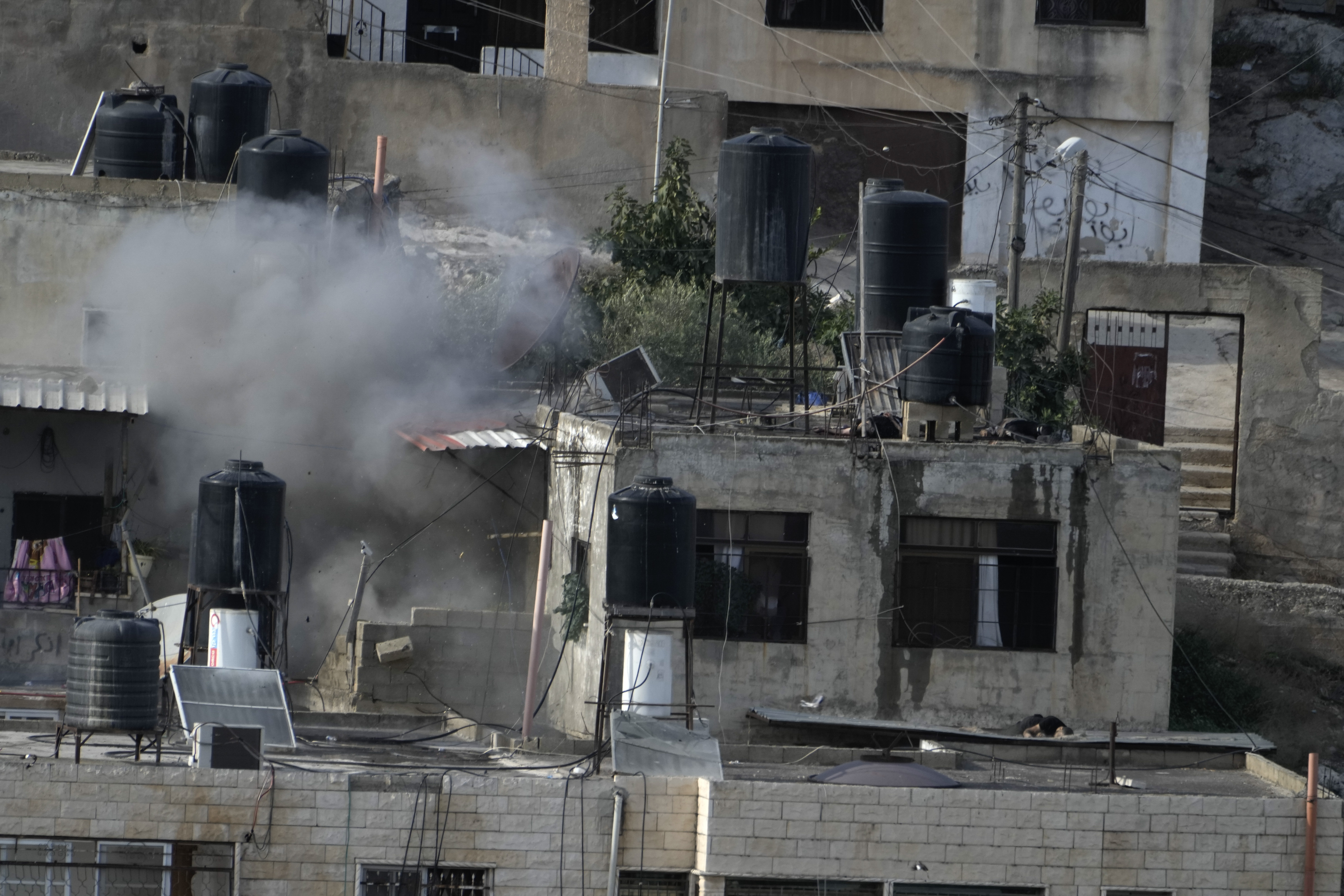 EDS NOTE: GRAPHIC CONTENT - An explosion is seen as three bodies lie motionless on rooftops in the West Bank town of in the West Bank town of Qabatiya during a raid, Thursday, Sept. 19, 2024. (AP Photo/Majdi Mohammed)