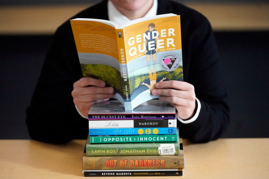 FILE - Amanda Darrow, director of youth, family and education programs at the Utah Pride Center, poses with books that have been the subject of complaints from parents, including "Gender Queer" by Meir Kobabe, on Dec. 16, 2021, in Salt Lake City. (AP Photo/Rick Bowmer, File)