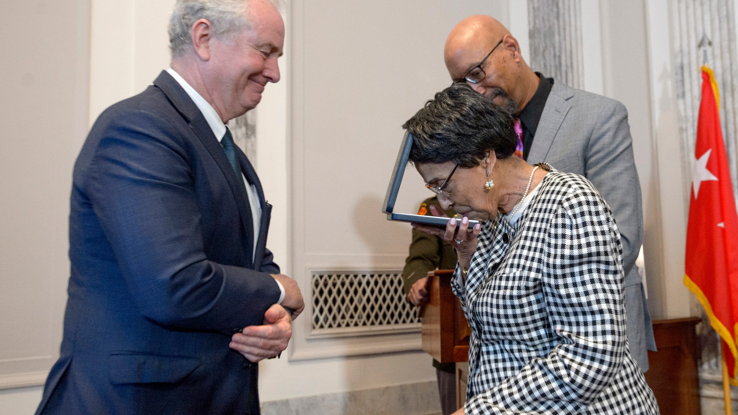 Joann Woodson, center, kisses the Distinguished Service Cross while Sen. Chris Van Hollen, D-Md., left, and her son Steve Woodson, right, watch during a ceremony to posthumously award the Distinguished Service Cross to her husband U.S. Army Staff Sgt. Waverly Woodson, Jr., a medic who was part of the only Black combat unit to take part in the D-Day invasion of France during World War II, on Capitol Hill, in Washington, Tuesday, Sept. 24, 2024. (AP Photo/Rod Lamkey, Jr.)