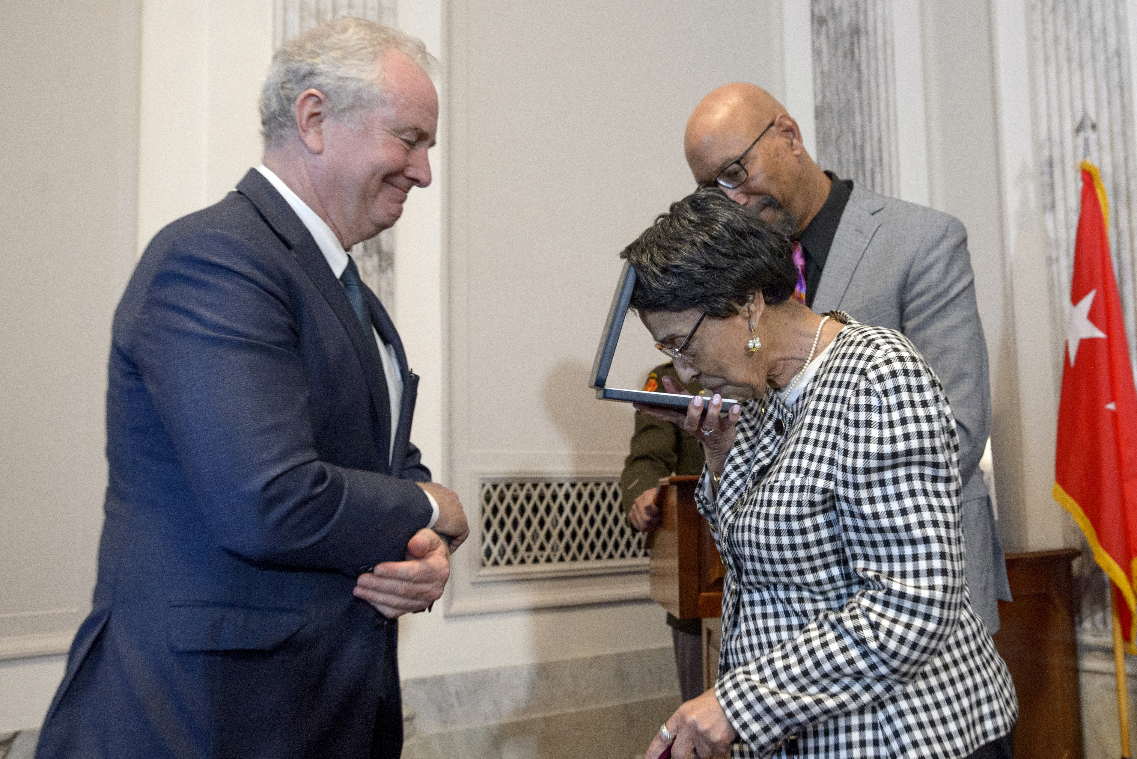 Joann Woodson, center, kisses the Distinguished Service Cross while Sen. Chris Van Hollen, D-Md., left, and her son Steve Woodson, right, watch during a ceremony to posthumously award the Distinguished Service Cross to her husband U.S. Army Staff Sgt. Waverly Woodson, Jr., a medic who was part of the only Black combat unit to take part in the D-Day invasion of France during World War II, on Capitol Hill, in Washington, Tuesday, Sept. 24, 2024. (AP Photo/Rod Lamkey, Jr.)