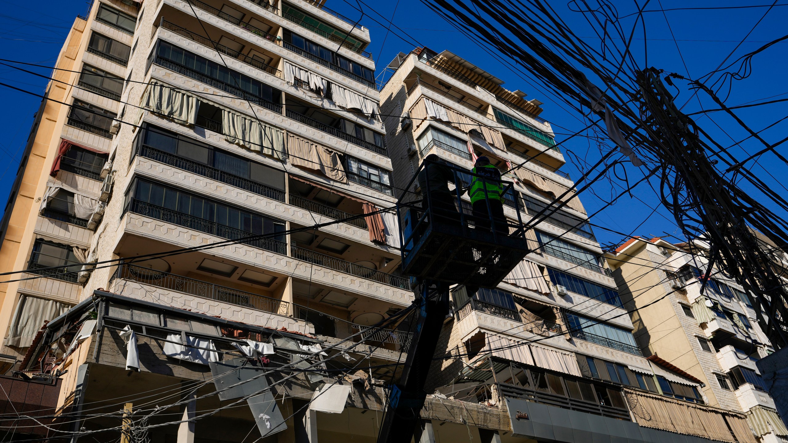 Municipality workers remove power cables in front of damaged buildings at the site of an Israeli airstrike in Beirut's southern suburb, Thursday, Sept. 26, 2024. (AP Photo/Hassan Ammar)