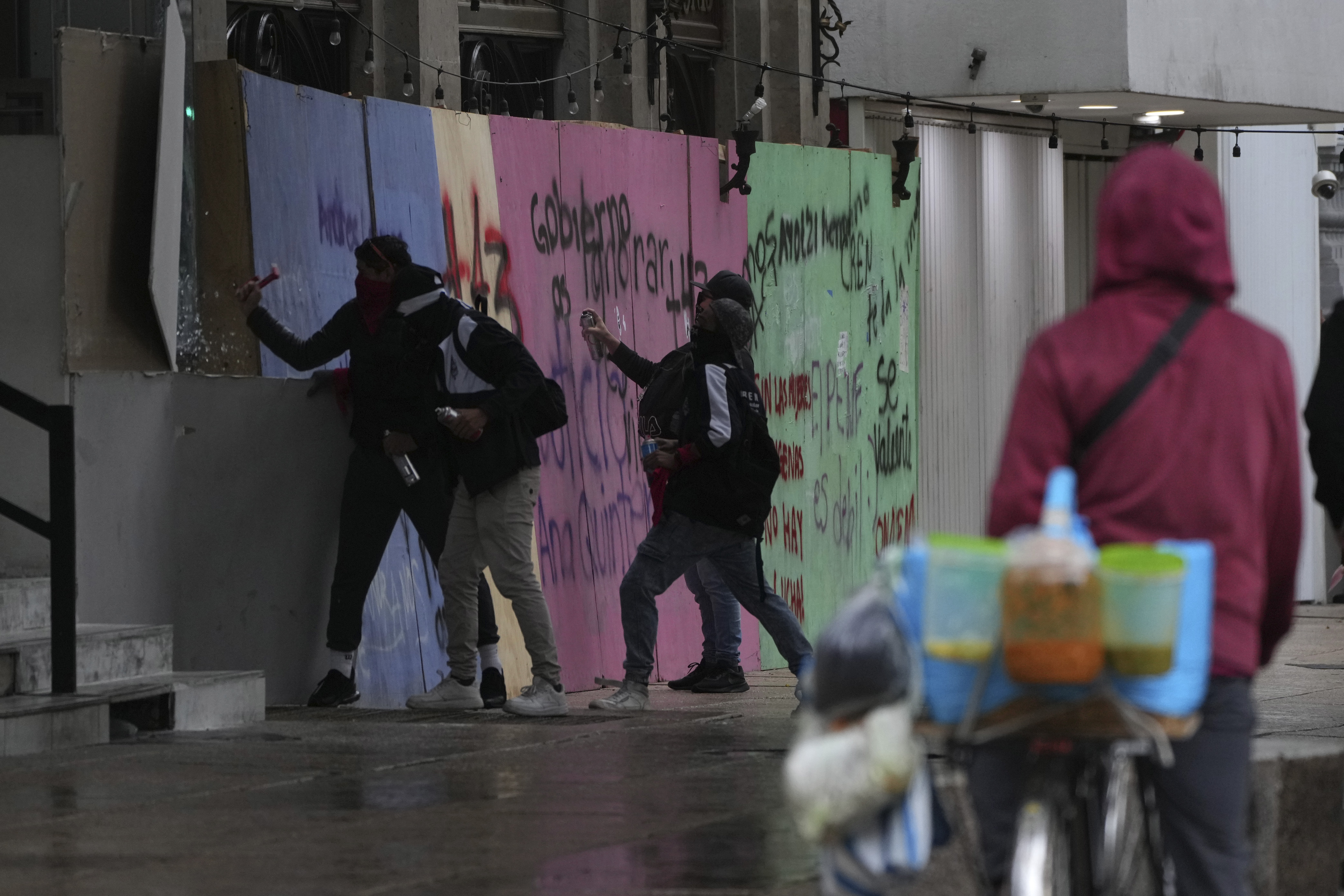 Masked youths crack a window as others spray paint anti-government slogans on a barrier protecting a storefront restaurant during a march marking the 10-year anniversary of the disappearance of 43 students from an Ayotzinapa rural teacher's college, in Mexico City, Thursday, Sept. 26, 2024. (AP Photo/Fernando Llano)