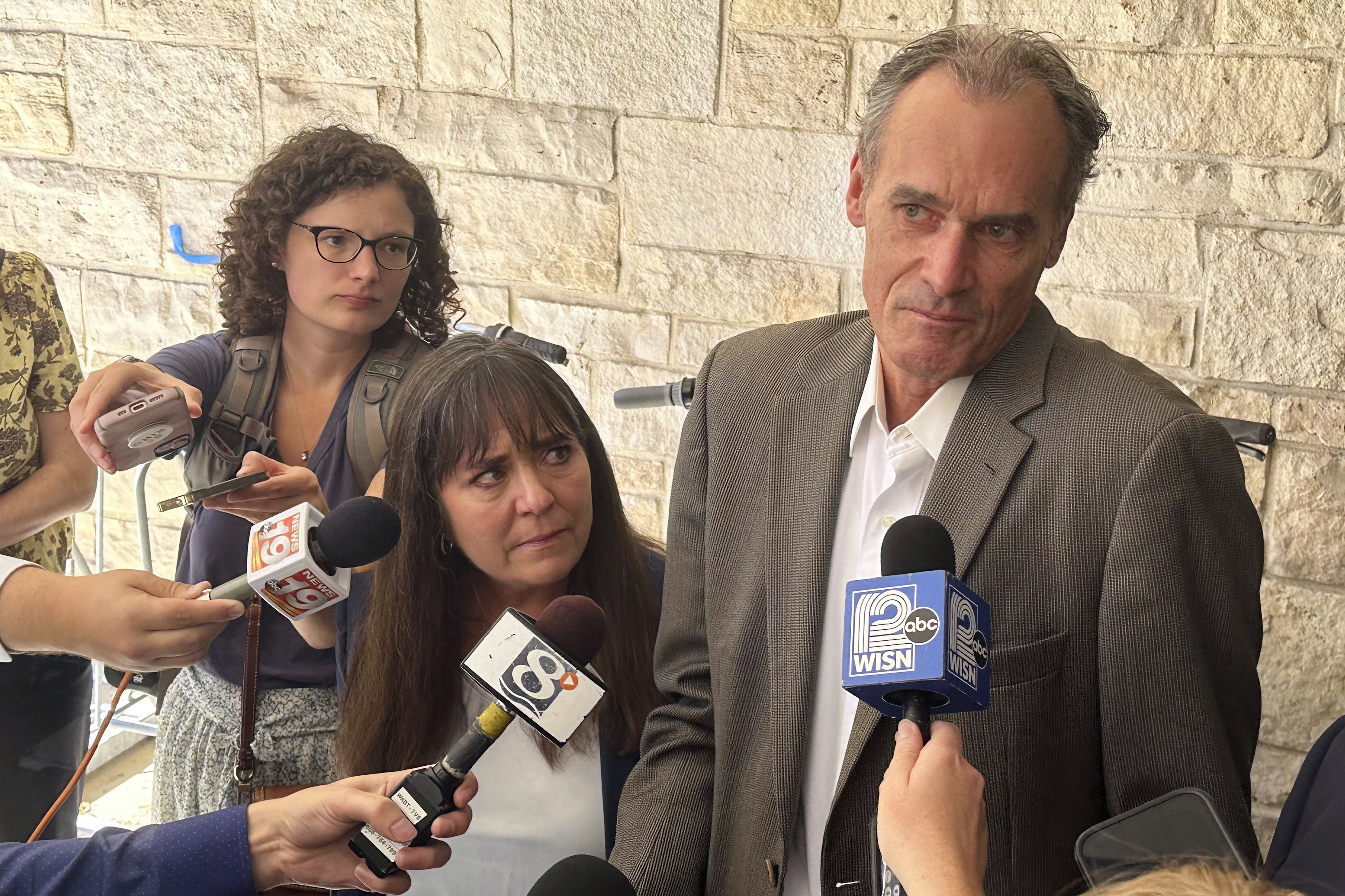 Former University of Wisconsin-La Crosse Chancellor Joe Gow, right, and his wife, Carmen Wilson, center, take questions after a hearing before a committee that will determine whether he can teach after being fired as the campus leader for making pornographic videos, Friday, Sept. 20, 2024, in Madison, Wis. (AP Photo/Scott Bauer)