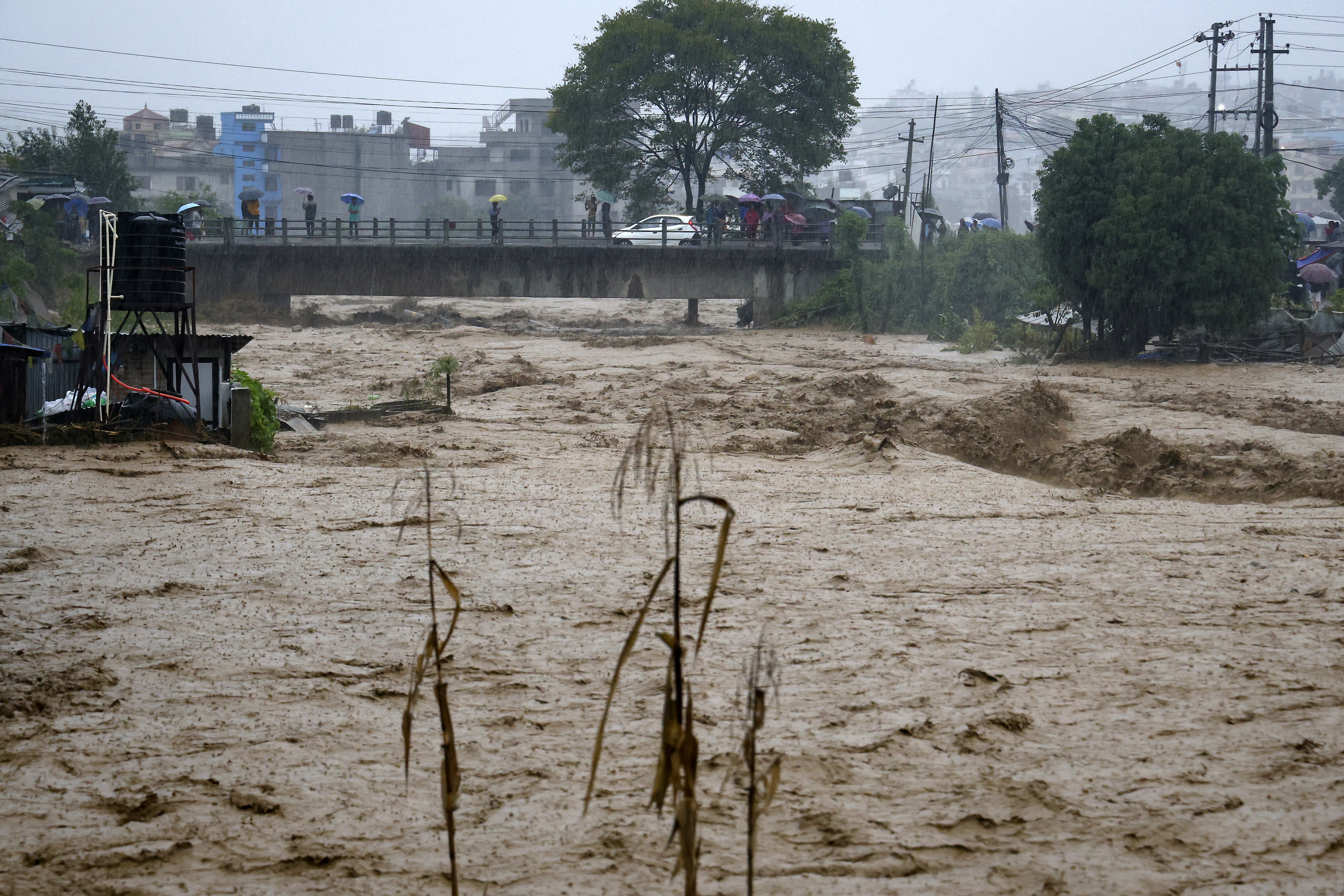 People watch the turbulent waters of Bagmati River from a bridge as the river flooded due to heavy rains in Kathmandu, Nepal, Saturday, Sept. 28, 2024. (AP Photo/Gopen Rai)