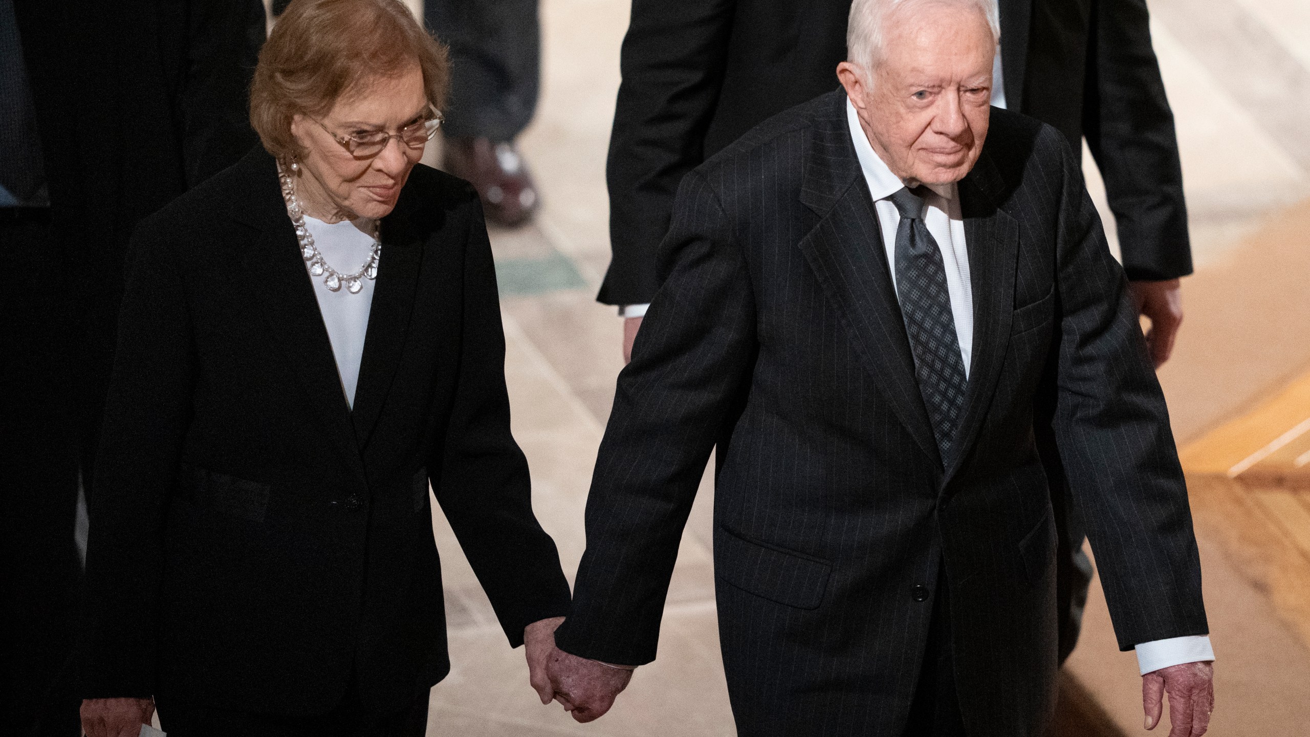 FILE - Former President Jimmy Carter, right, and his wife, former first lady Rosalynn Carter, hold hands as they walk from a state funeral for former President George H.W. Bush at the National Cathedral, Dec. 5, 2018, in Washington. (AP Photo/Carolyn Kaster, File)