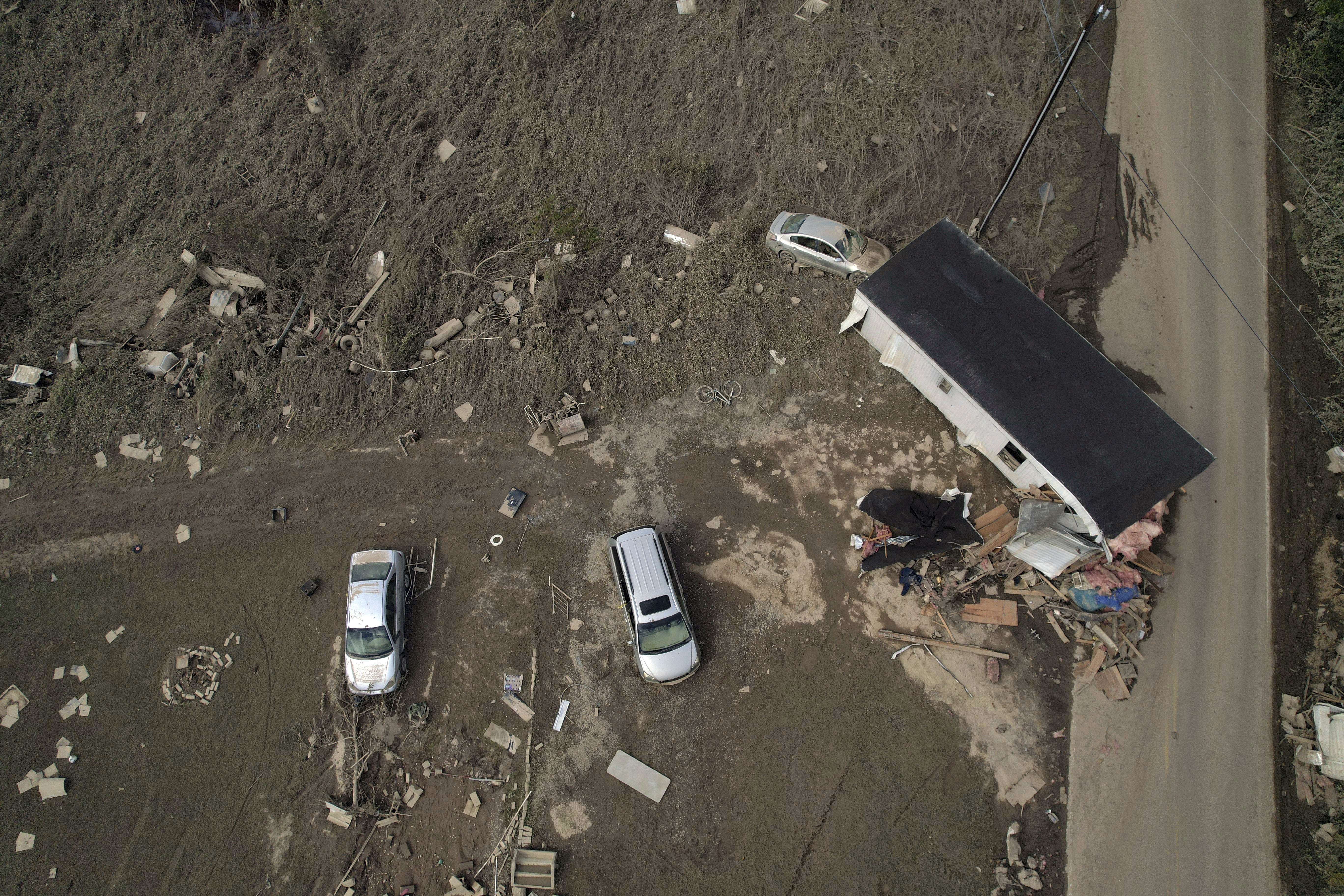 A destroyed mobile home and vehicles lay scattered across muddy land, Tuesday, Oct. 1, 2024, in Hendersonville, N.C., in the aftermath of Hurricane Helene. (AP Photo/Brittany Peterson)