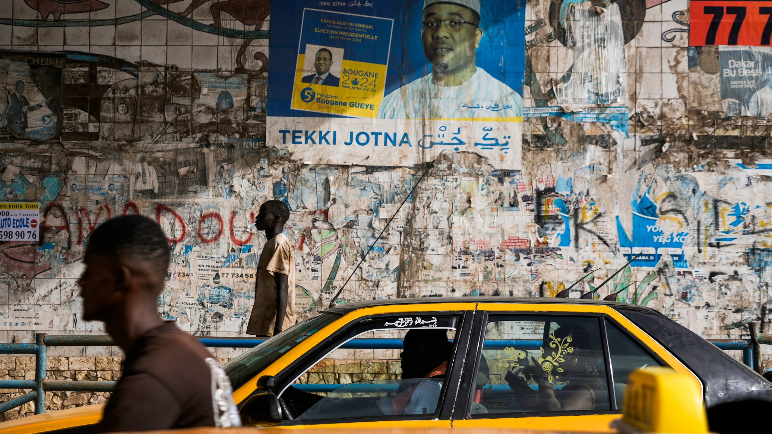 A man walks in front of posters written in Wolof in Dakar, Senegal, Wednesday, Oct. 2, 2024. (AP Photo/Annie Risemberg)