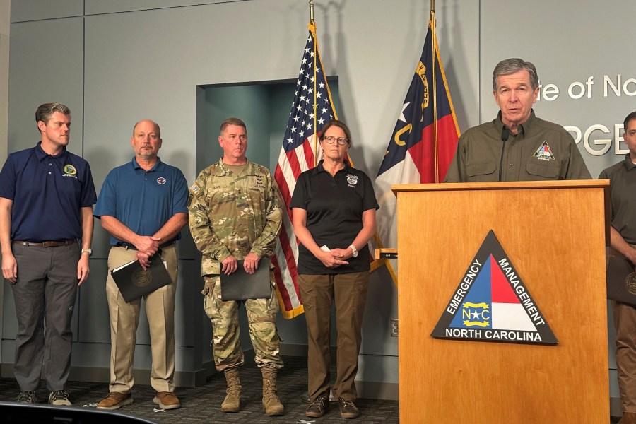 North Carolina Gov. Roy Cooper, right at podium, speaks during a media briefing on the government response to Hurricane Helene in western North Carolina while Federal Emergency Management Agency Administrator Deanne Criswell, center, and others listen at the state Emergency Operations Center in Raleigh, N.C., Tuesday, Oct. 1, 2024. (AP Photo/Gary D. Robertson)