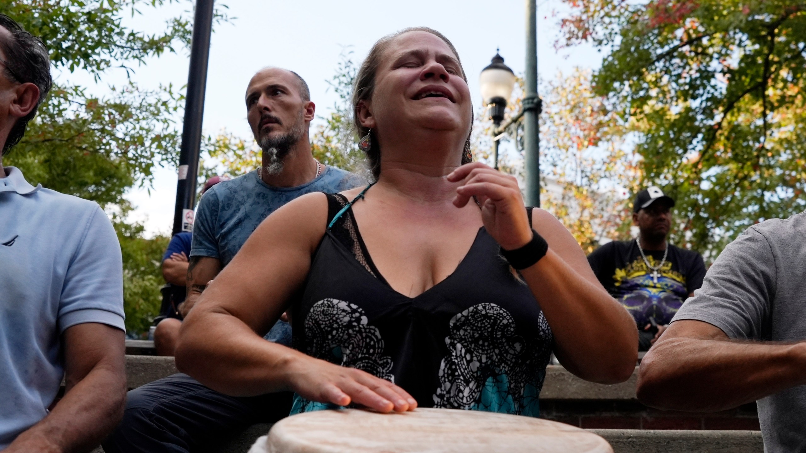 A woman plays music at a drum circle Friday, Oct. 4, 2024 in Asheville, N.C., a week after Hurricane Helene upended lives across the Southeast. (AP Photo/Brittany Peterson)