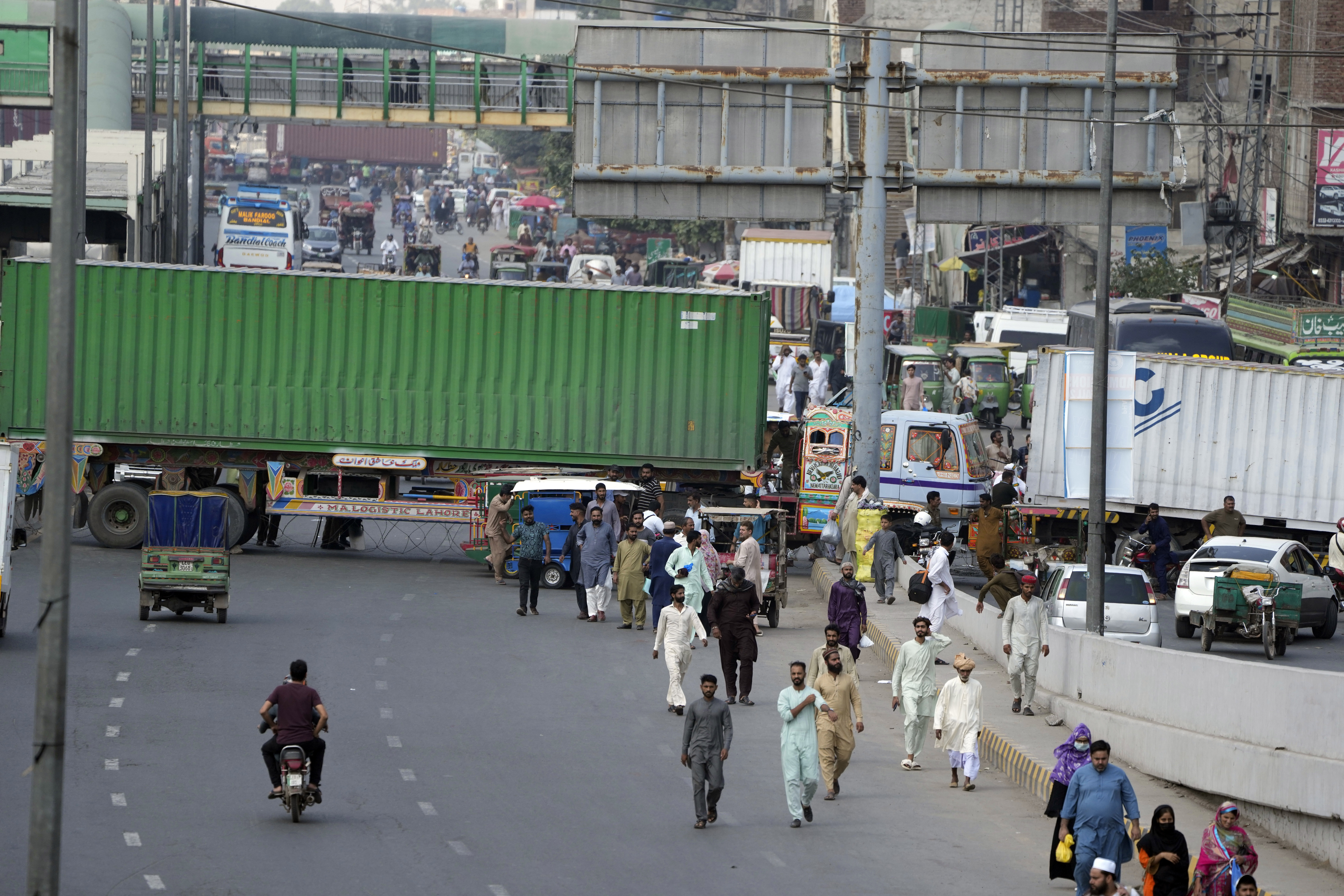 People try to cross through shipping containers set up by authorities to prevent supporters of imprisoned former Prime Minister Imran Khan from holding a rally to demand his release in Lahore, Pakistan, Saturday, Oct. 5, 2024. (AP Photo/K.M. Chaudary)