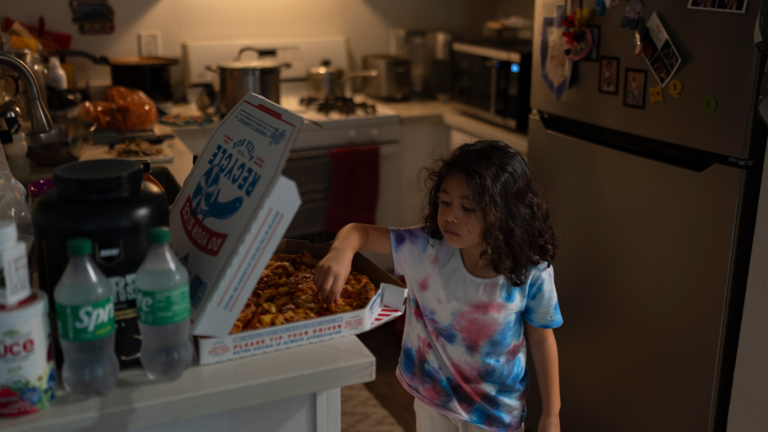 Rubie Caceres, a granddaughter of Marina Maalouf, a longtime resident of Hillside Villa, grabs a slice of pizza in her apartment in Los Angeles, Tuesday, Oct. 1, 2024. (AP Photo/Jae C. Hong)